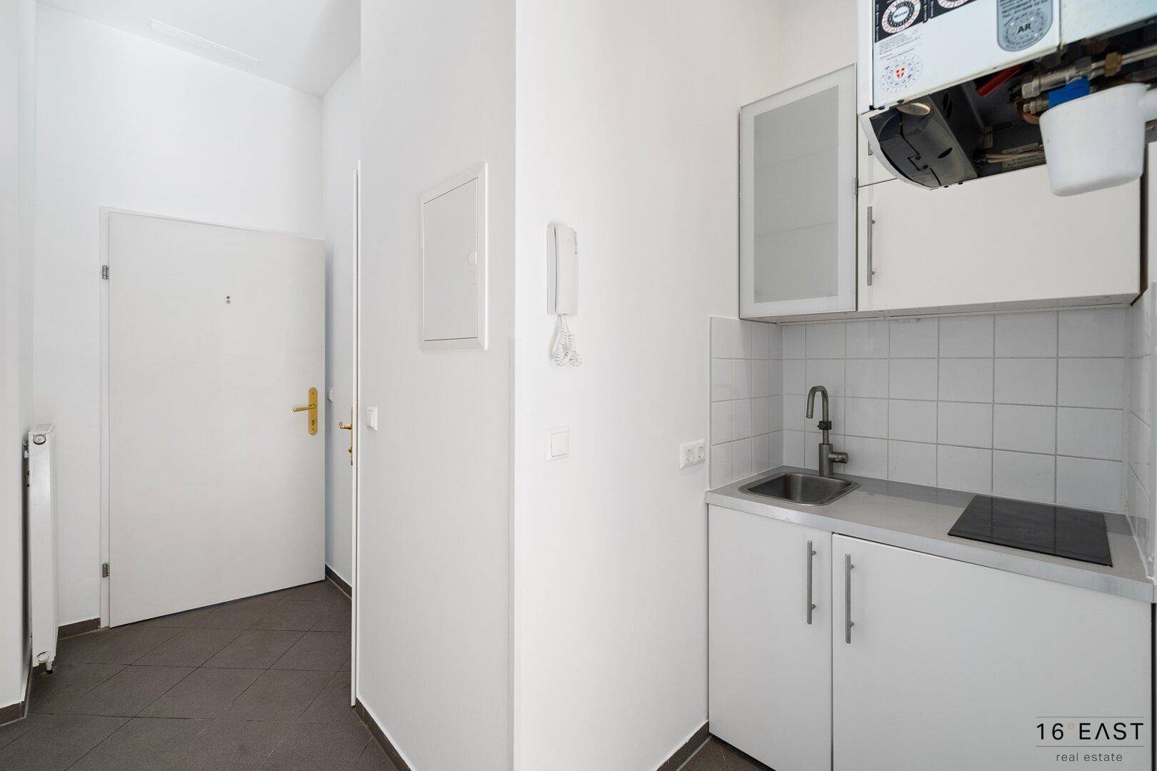 Kleine Küchenzeile mit Spüle und Kochfeld, integriert in einen hellen Eingangsbereich.