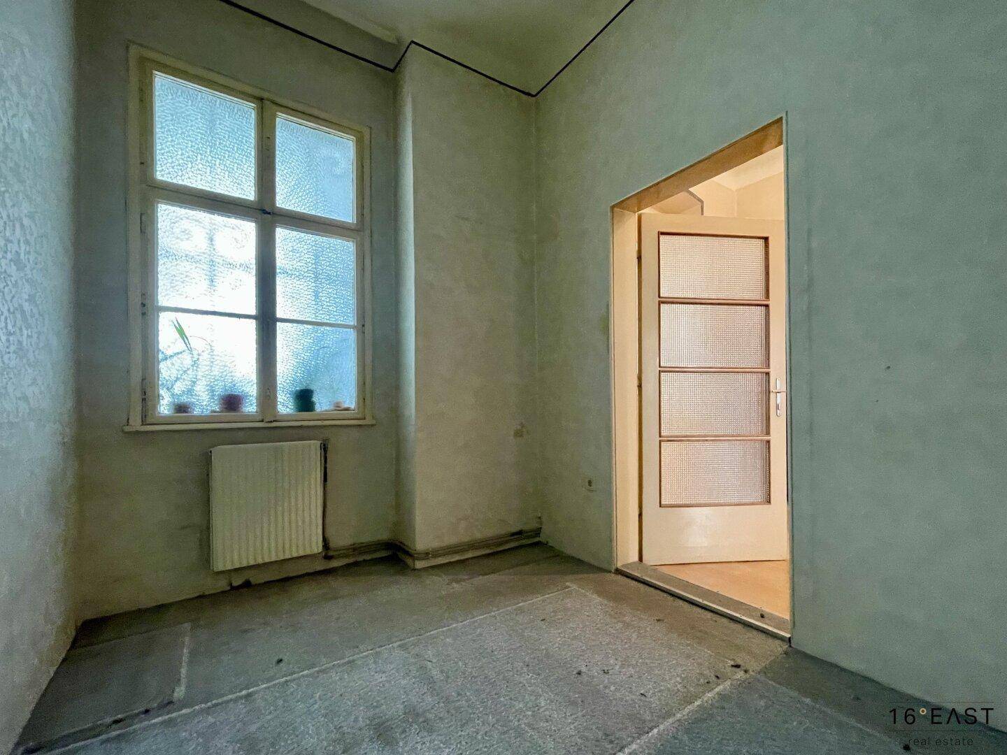 Kleiner, unmöblierter Raum mit Fenster und Tür, geeignet für verschiedene Nutzungen.