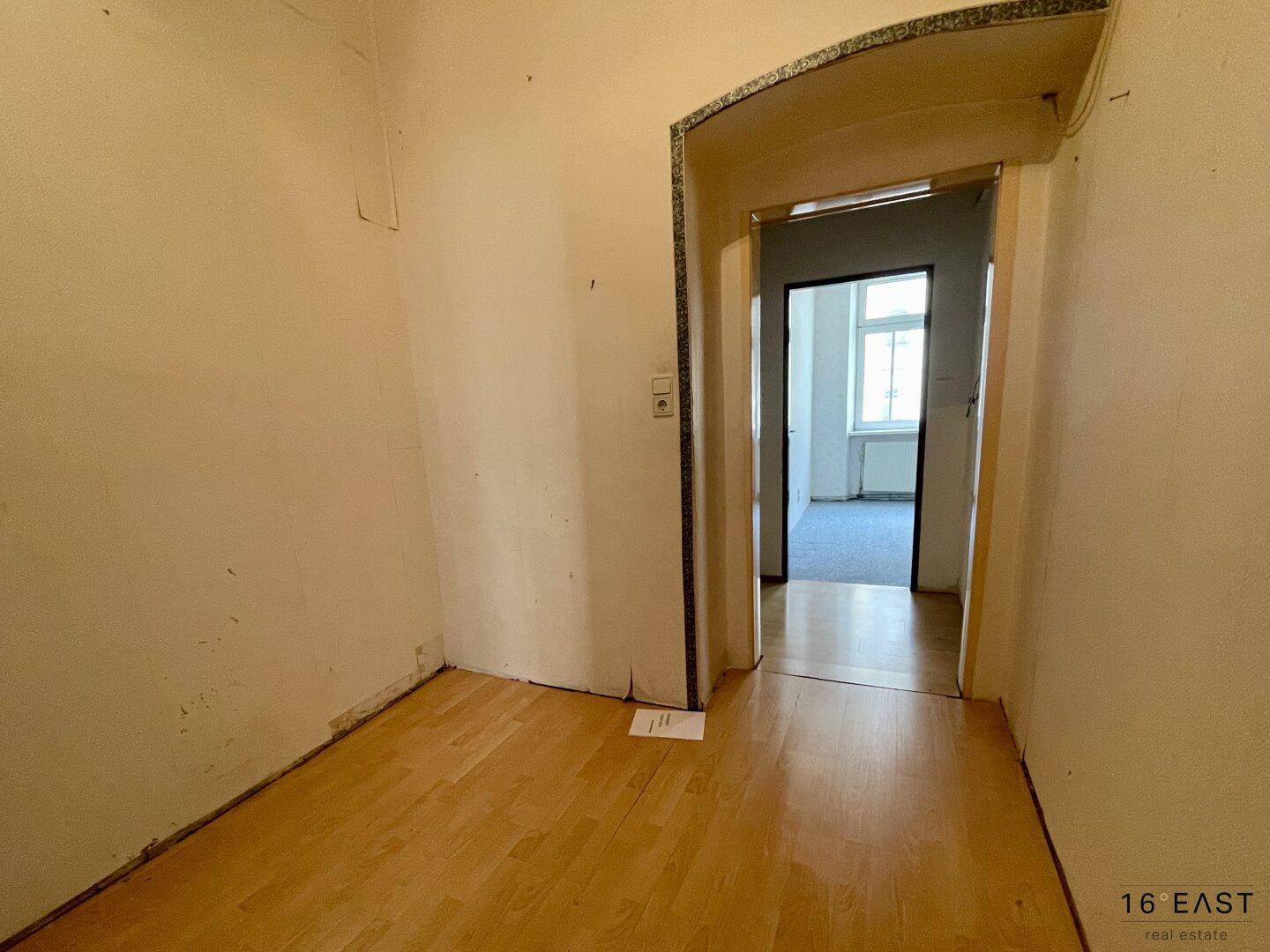 Leerer Raum mit Laminatboden und Durchgang zu einem weiteren Zimmer.