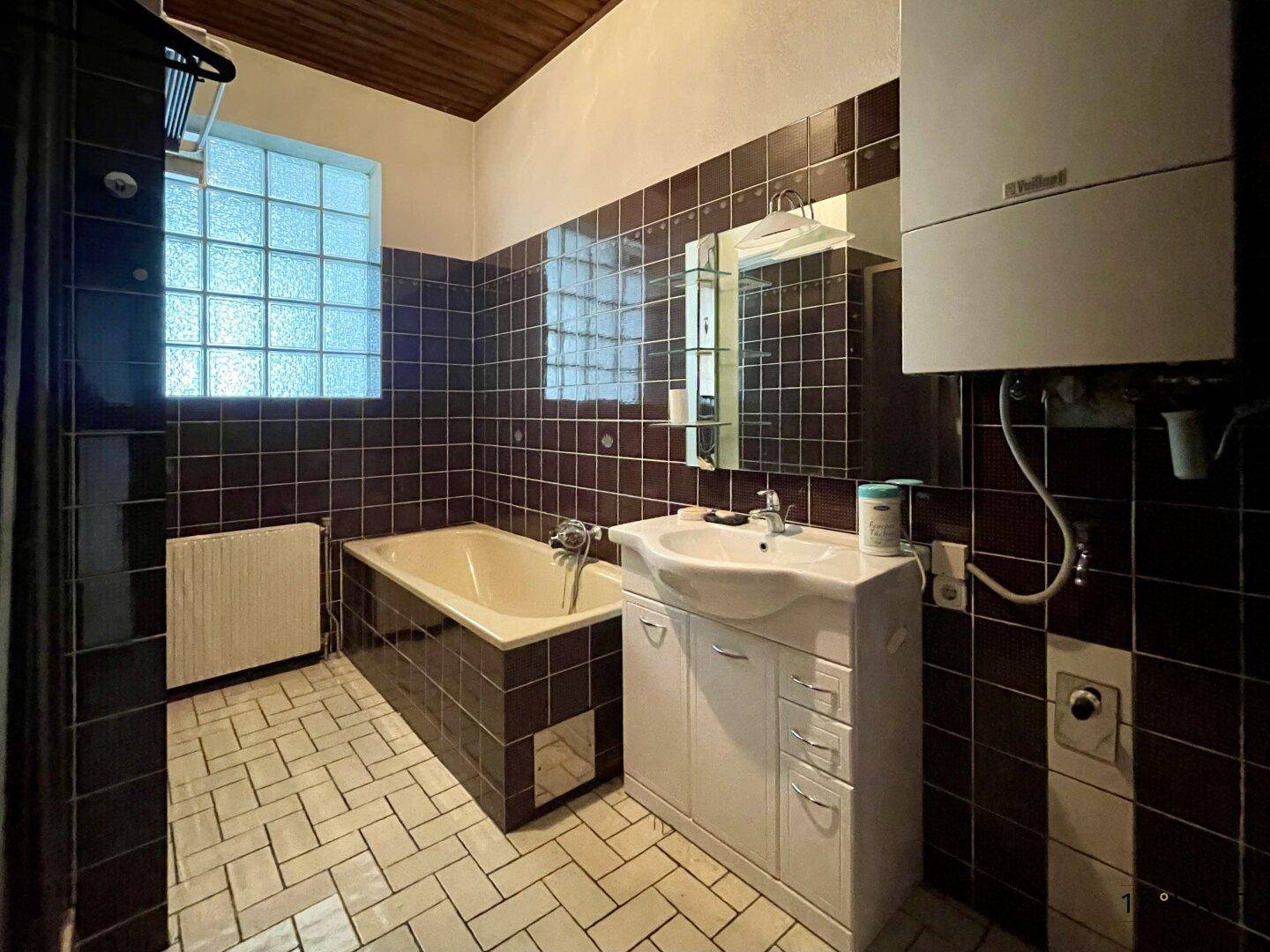 Badezimmer mit dunklen Fliesen, Badewanne, Waschbecken und Gastherme.