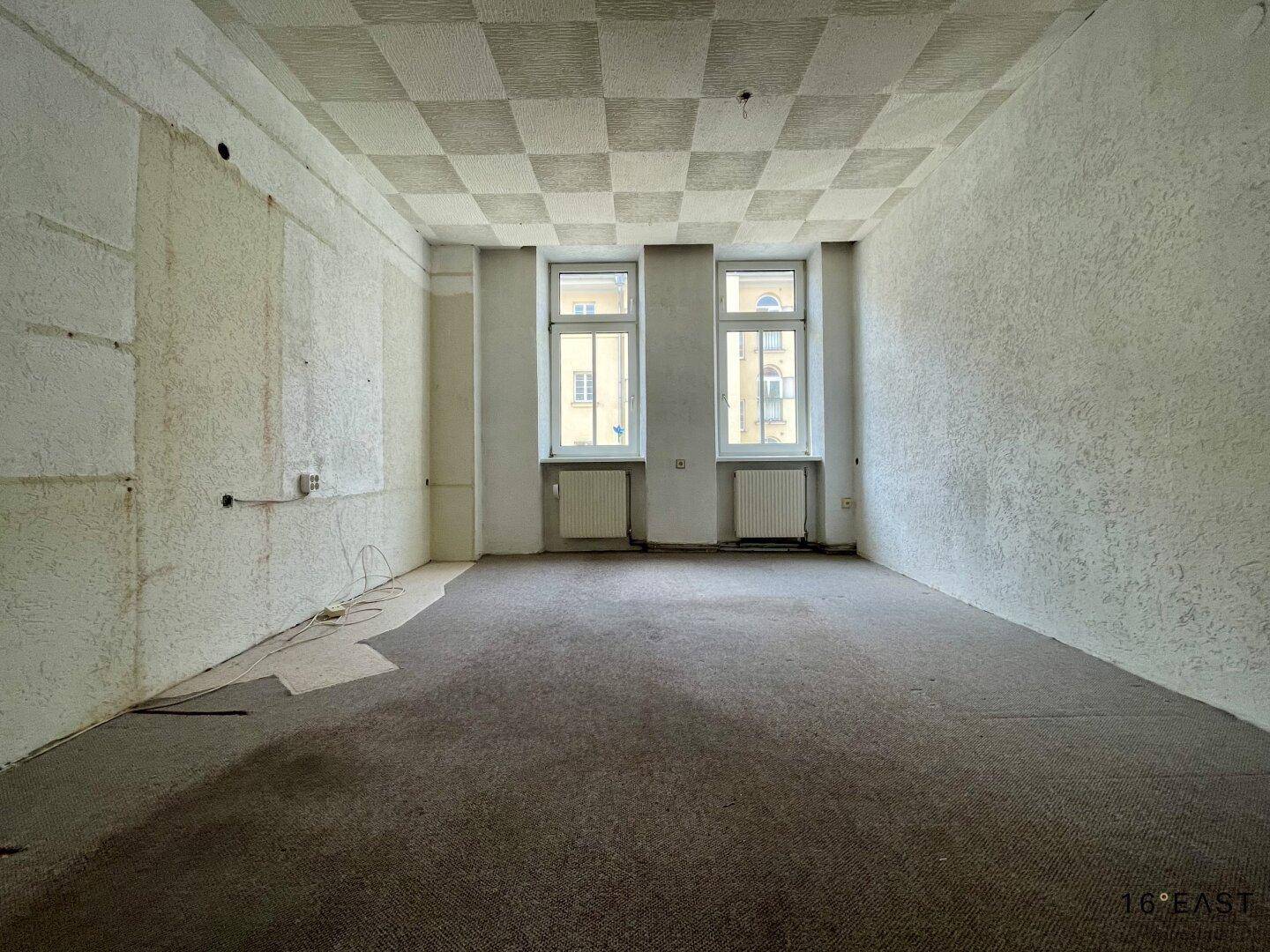Leerer Raum mit Teppichboden und vorbereiteten Wänden für eine bevorstehende Renovierung.