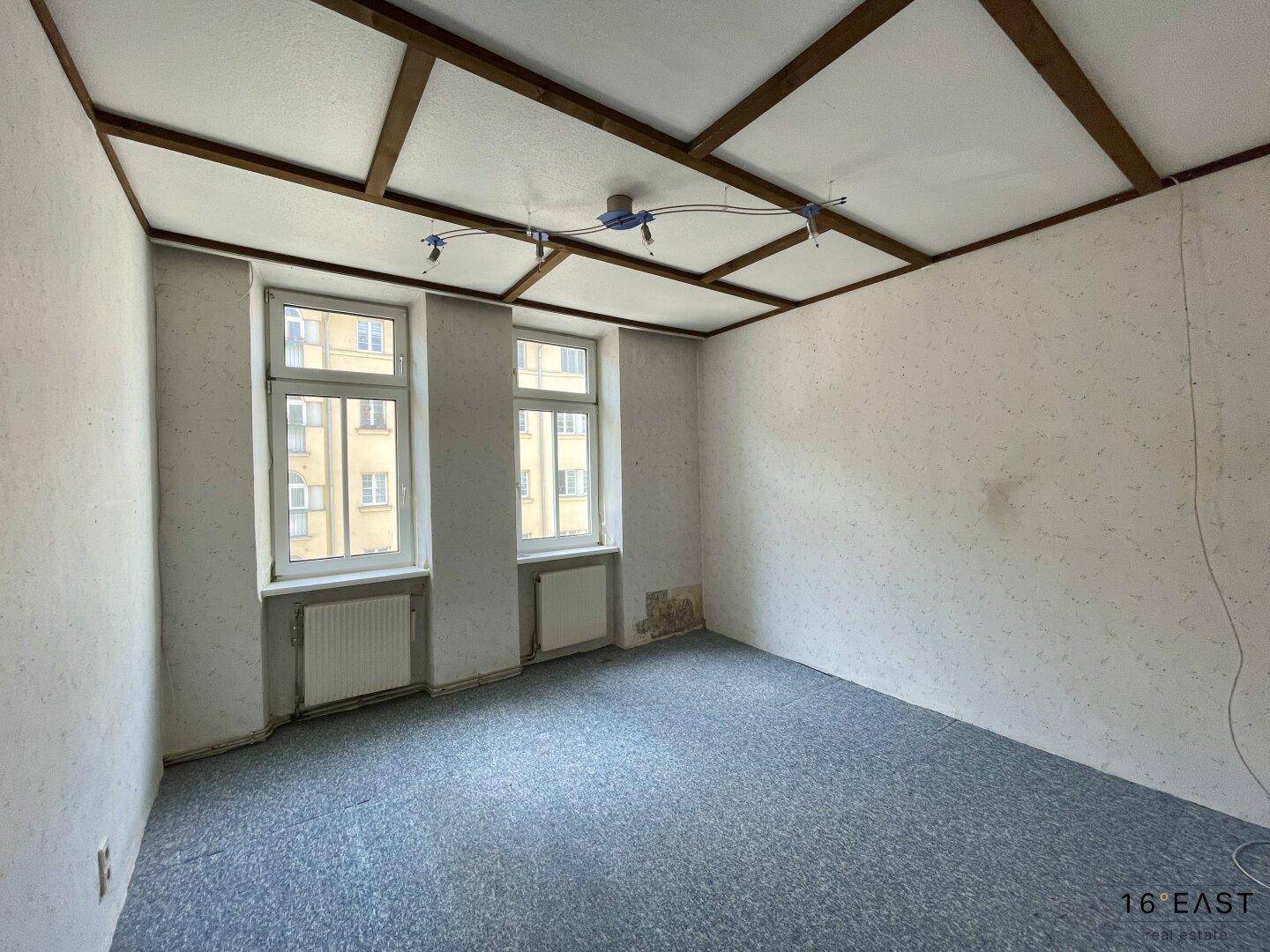 Leeres Zimmer mit blauem Teppichboden und Holzdeckenverkleidung, ideal als Schlafzimmer.