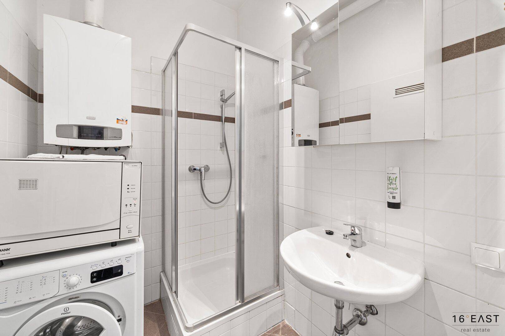 Kleines Badezimmer mit Dusche, Waschbecken und integrierter Waschmaschine.