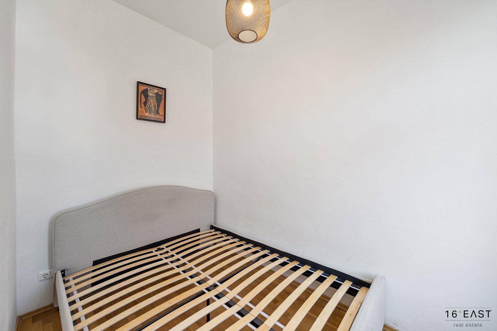 Einfaches Schlafzimmer mit Bettgestell und hellem Holzboden, bereit zur individuellen Gestaltung.