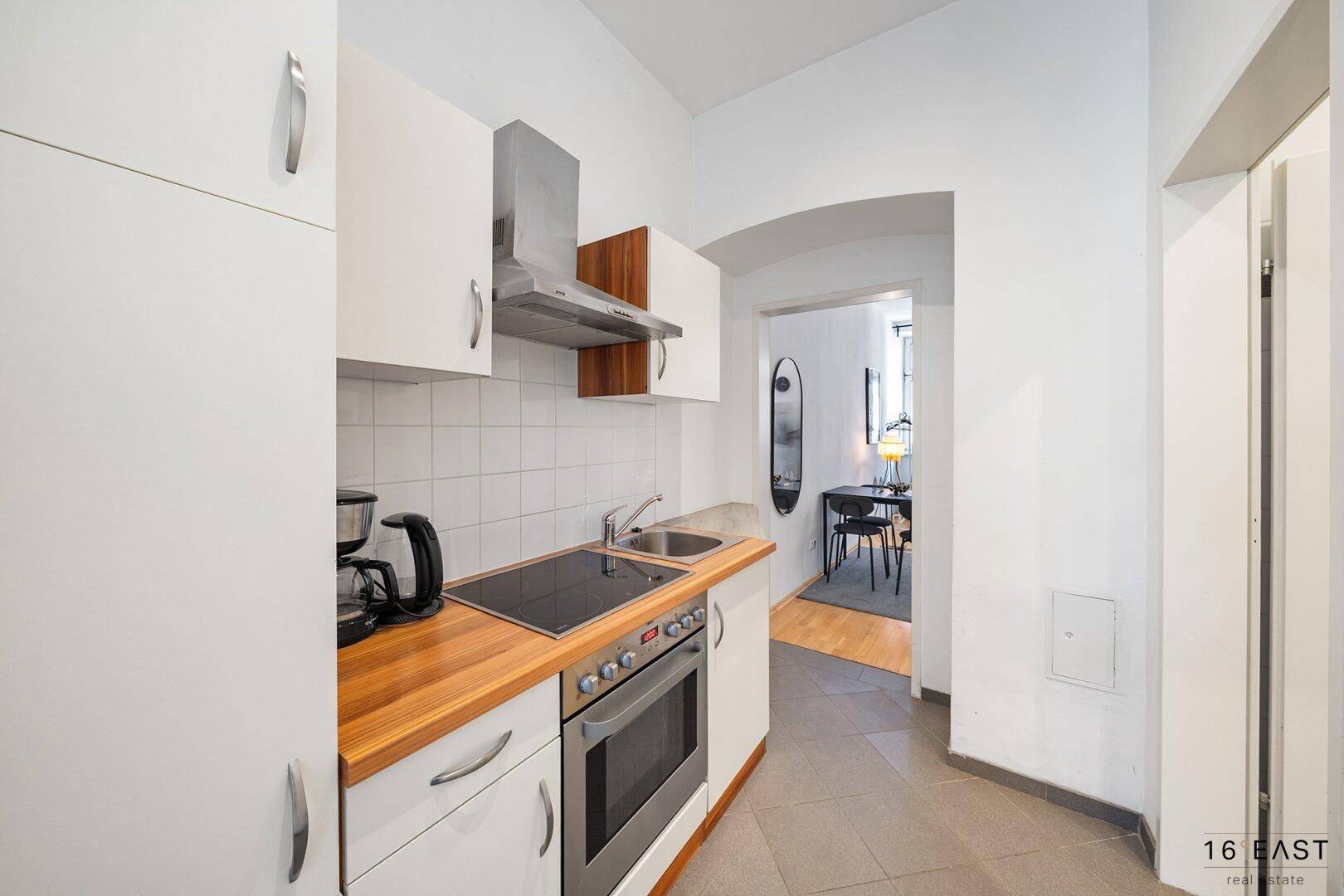 Funktionale Küche mit weißen Schränken, Holz-Arbeitsplatte und Blick in den Essbereich.