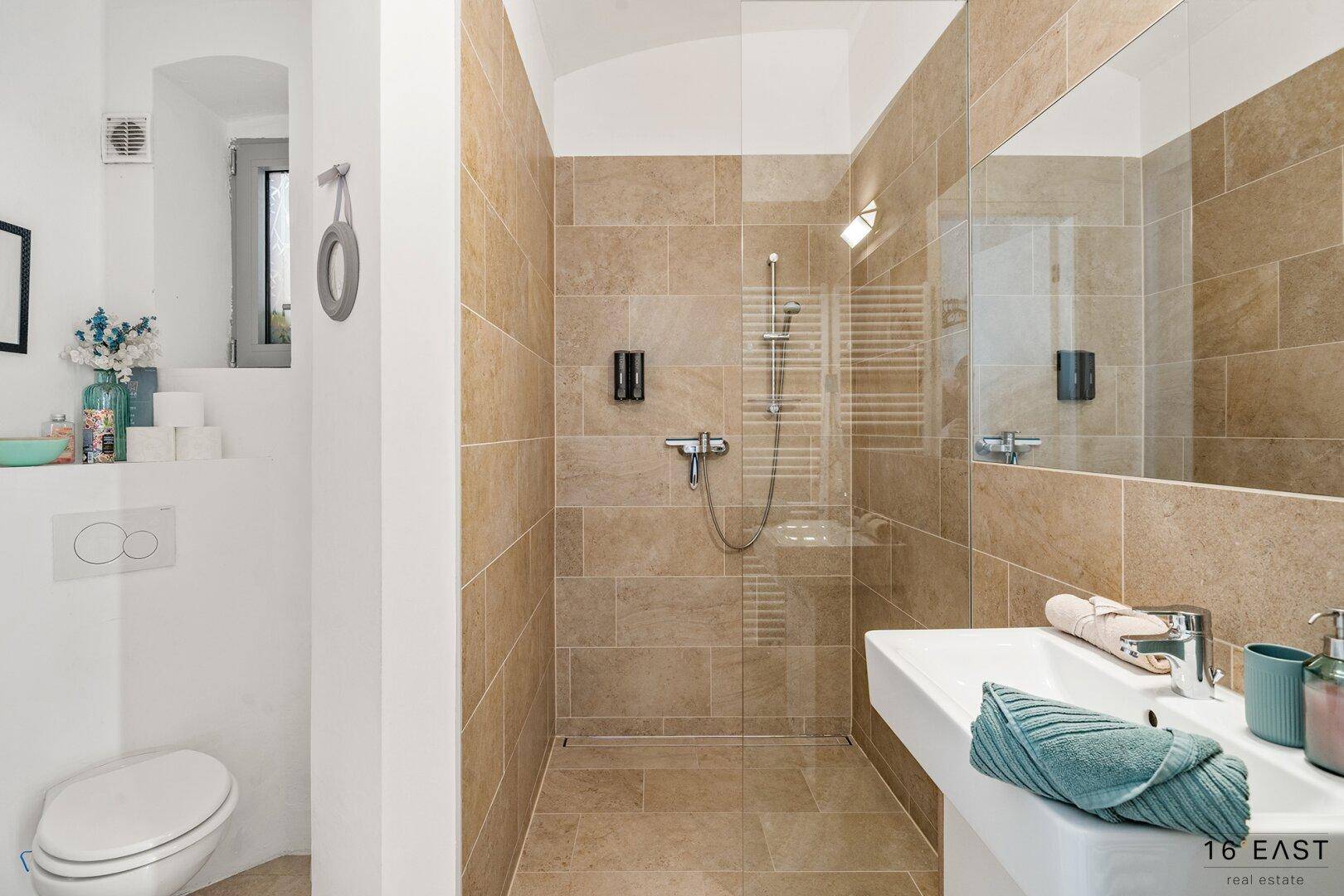 Modernes Badezimmer mit begehbarer Dusche und beigefarbenen Fliesen.
