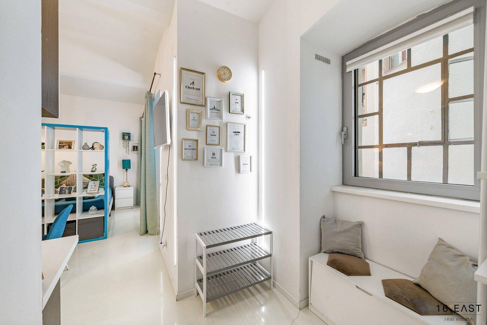 Heller Flur mit Fenster, Sitzbank und dekorativen Bilderrahmen an der Wand.