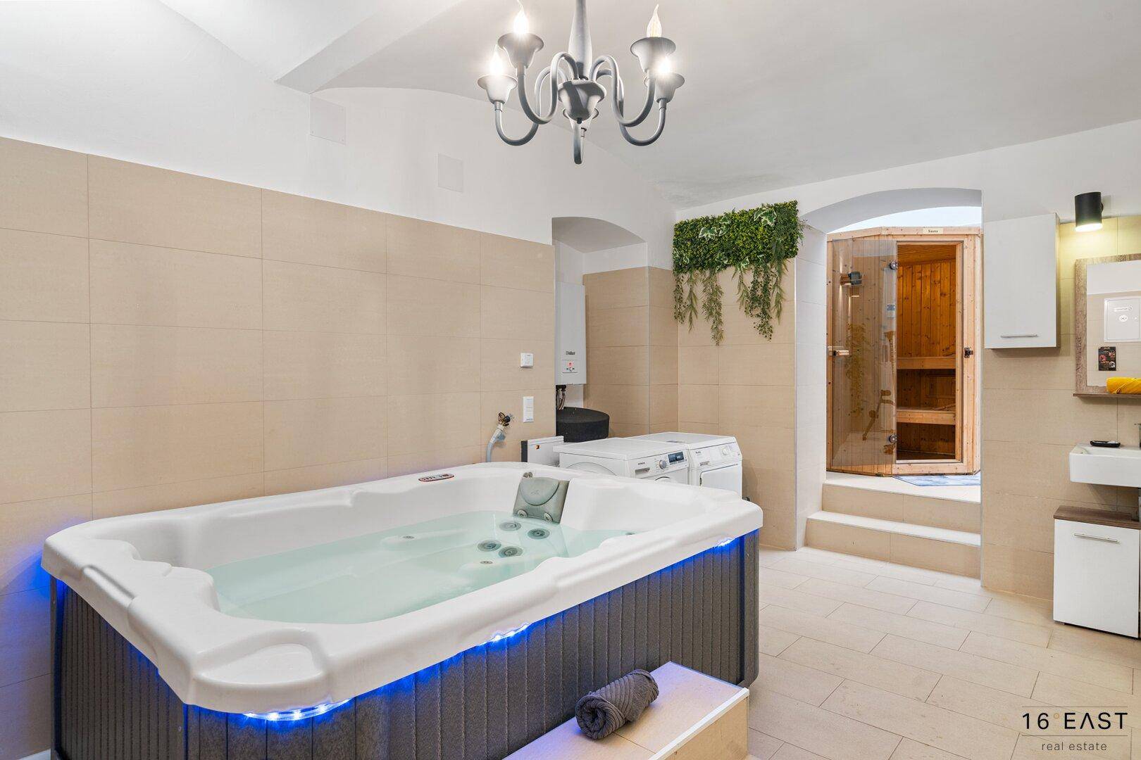 Wellnessbereich mit Whirlpool, Waschmaschine und Zugang zur Sauna.