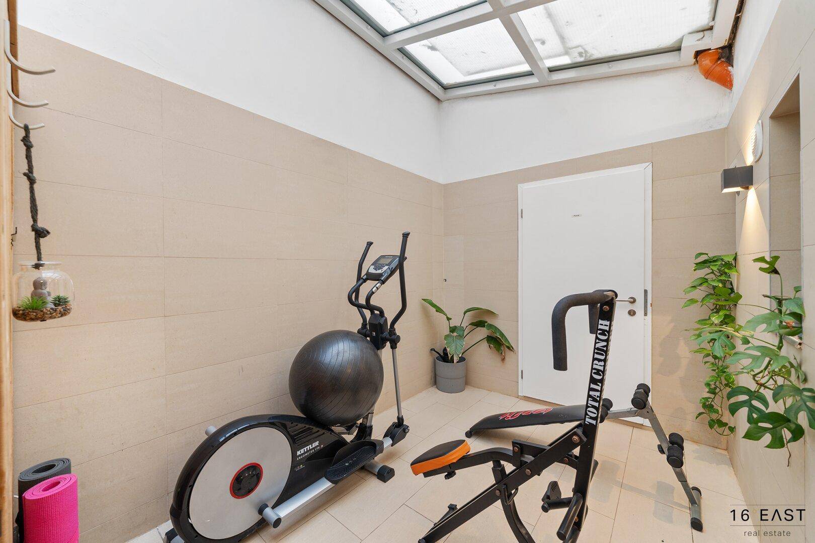 Fitnessbereich mit Trainingsgeräten und Oberlicht für natürliches Licht.