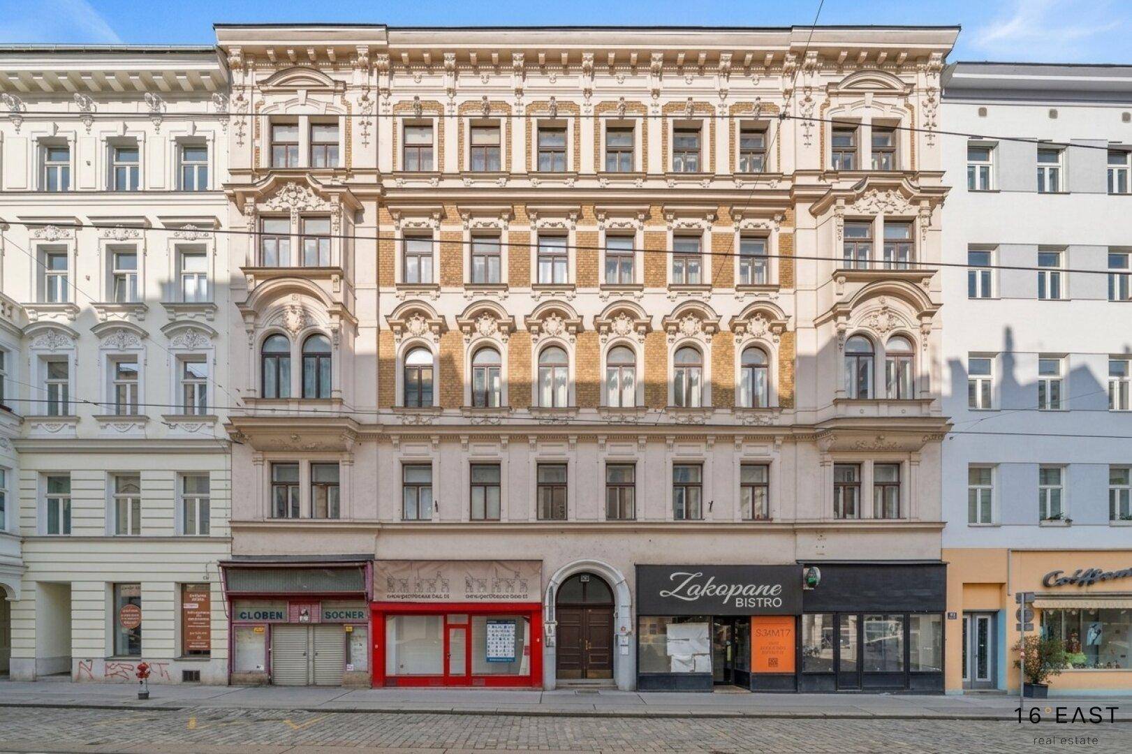 Historische Fassade eines Mehrfamilienhauses mit reich verzierten Details und Geschäften im Erdgeschoss.