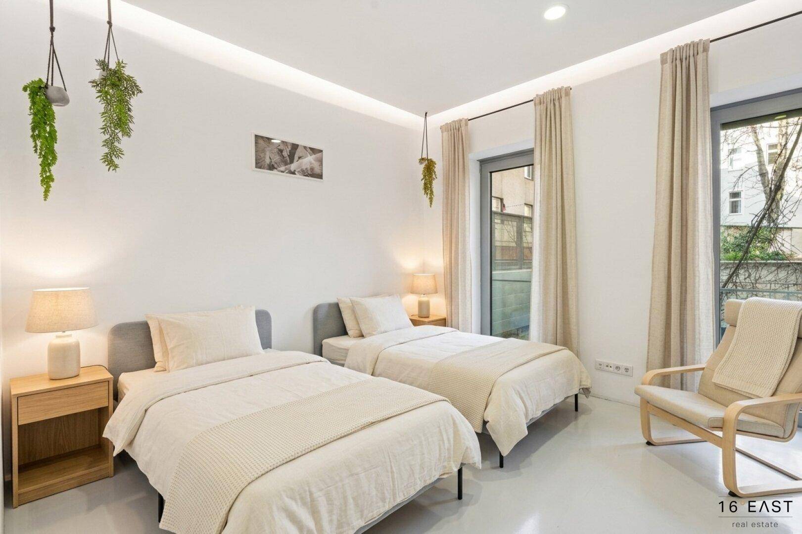 Helles Schlafzimmer mit zwei Einzelbetten, großen Fenstern und moderner Dekoration.