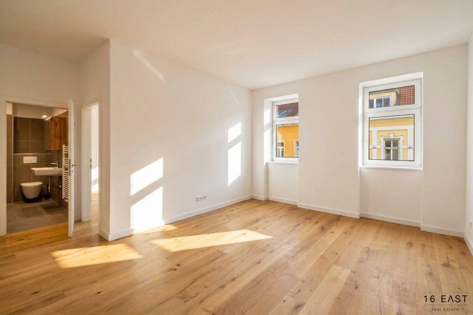 Heller Wohnraum mit neuem Holzfußboden, weißen Wänden und Zugang zu einem modernen Badezimmer.