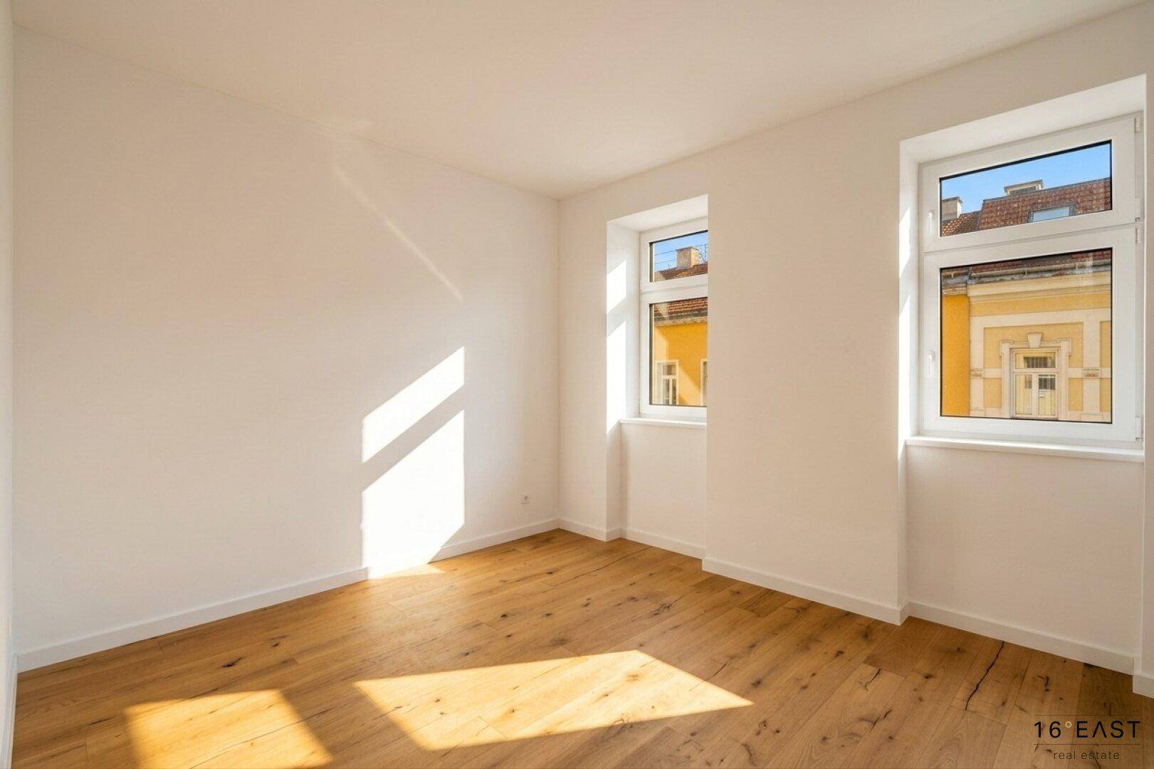 Sonniger Wohnraum mit hochwertigem Holzfußboden, weißen Wänden und Blick auf die Stadt.