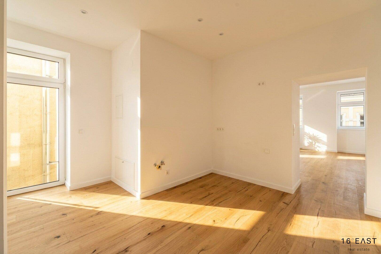 Lichtdurchfluteter Wohnraum mit Holzboden, weißen Wänden und Zugang zu einem Außenbereich.