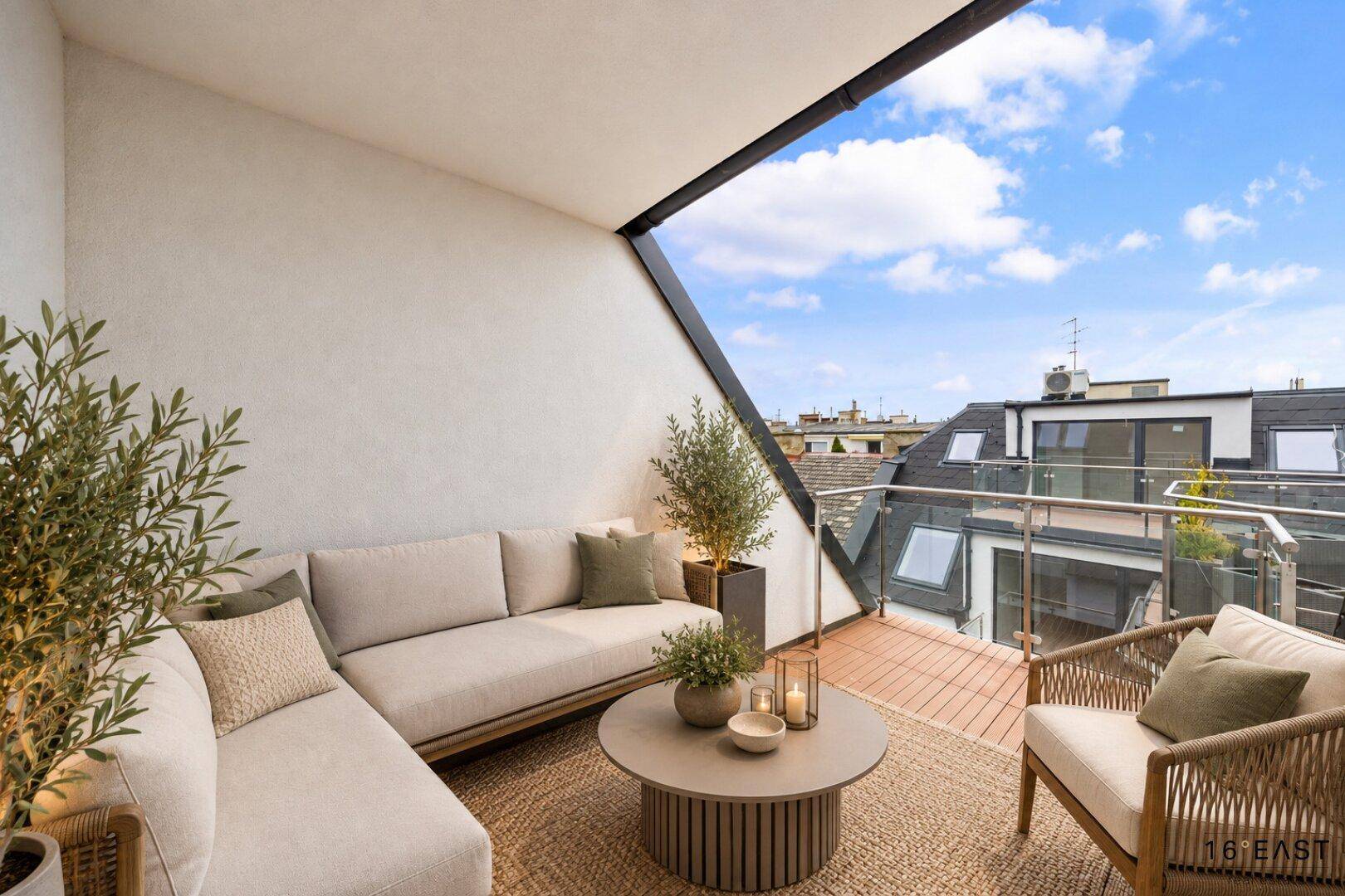 Moderner Balkon mit Holzboden, bequemen Loungemöbeln und Blick über die Dächer der Stadt.