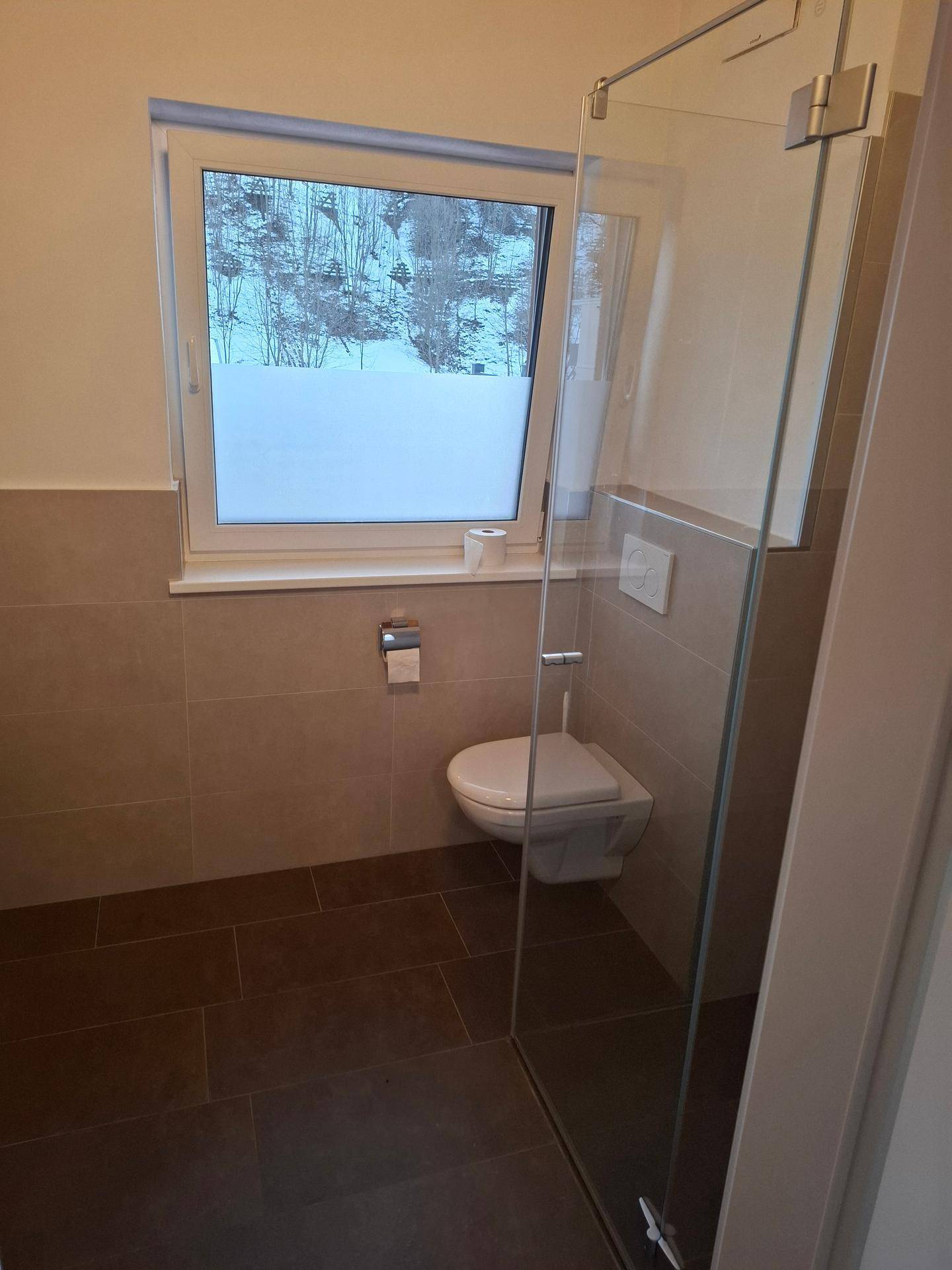Modernes Badezimmer mit wandhängendem WC, Duschkabine und Fenster.