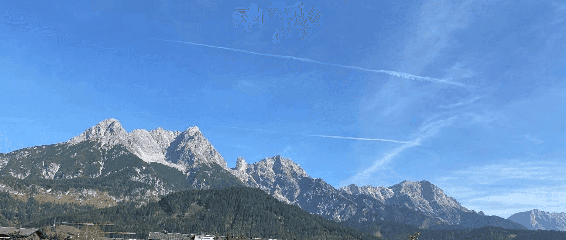 Panoramablick auf majestätische Berge unter einem klaren blauen Himmel mit Kondensstreifen.