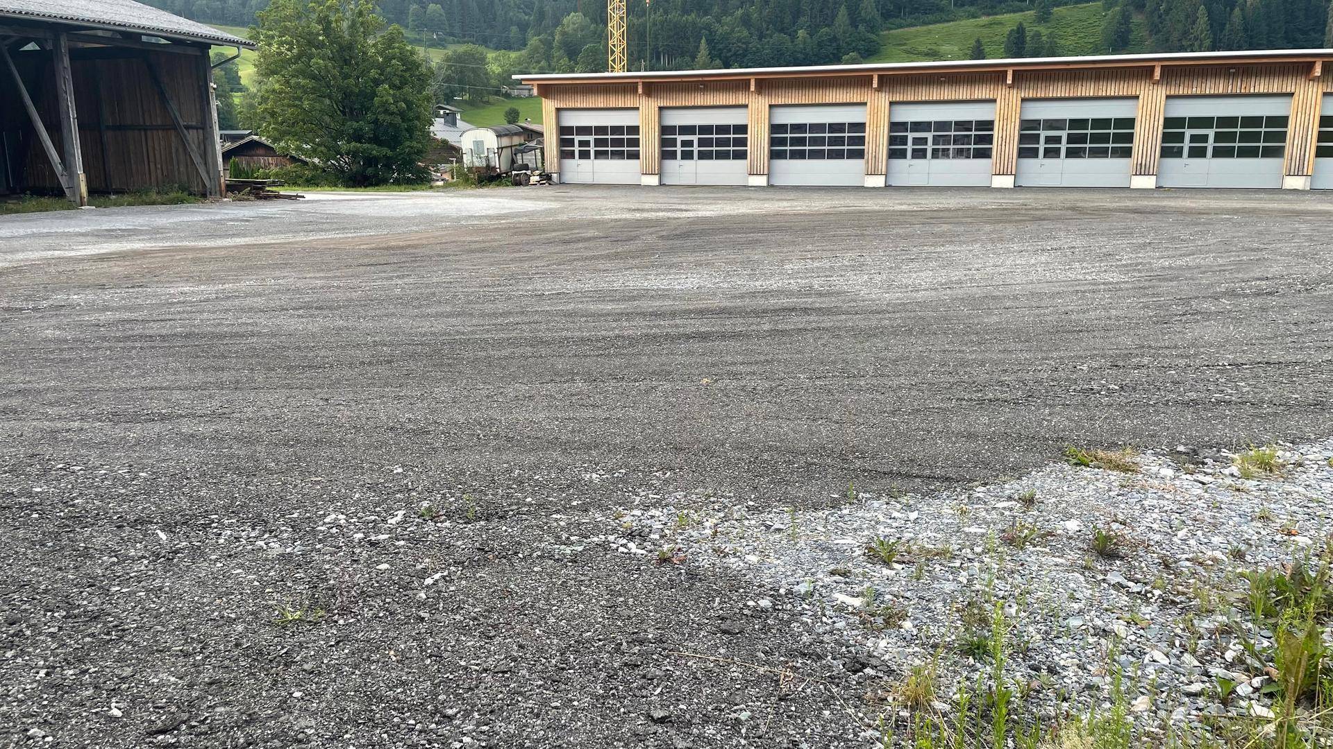Ausgedehnter Schotterbereich vor einem modernen Gebäude mit Holzfassade und mehreren Garagentoren, eingebettet in grüne Landschaft.
