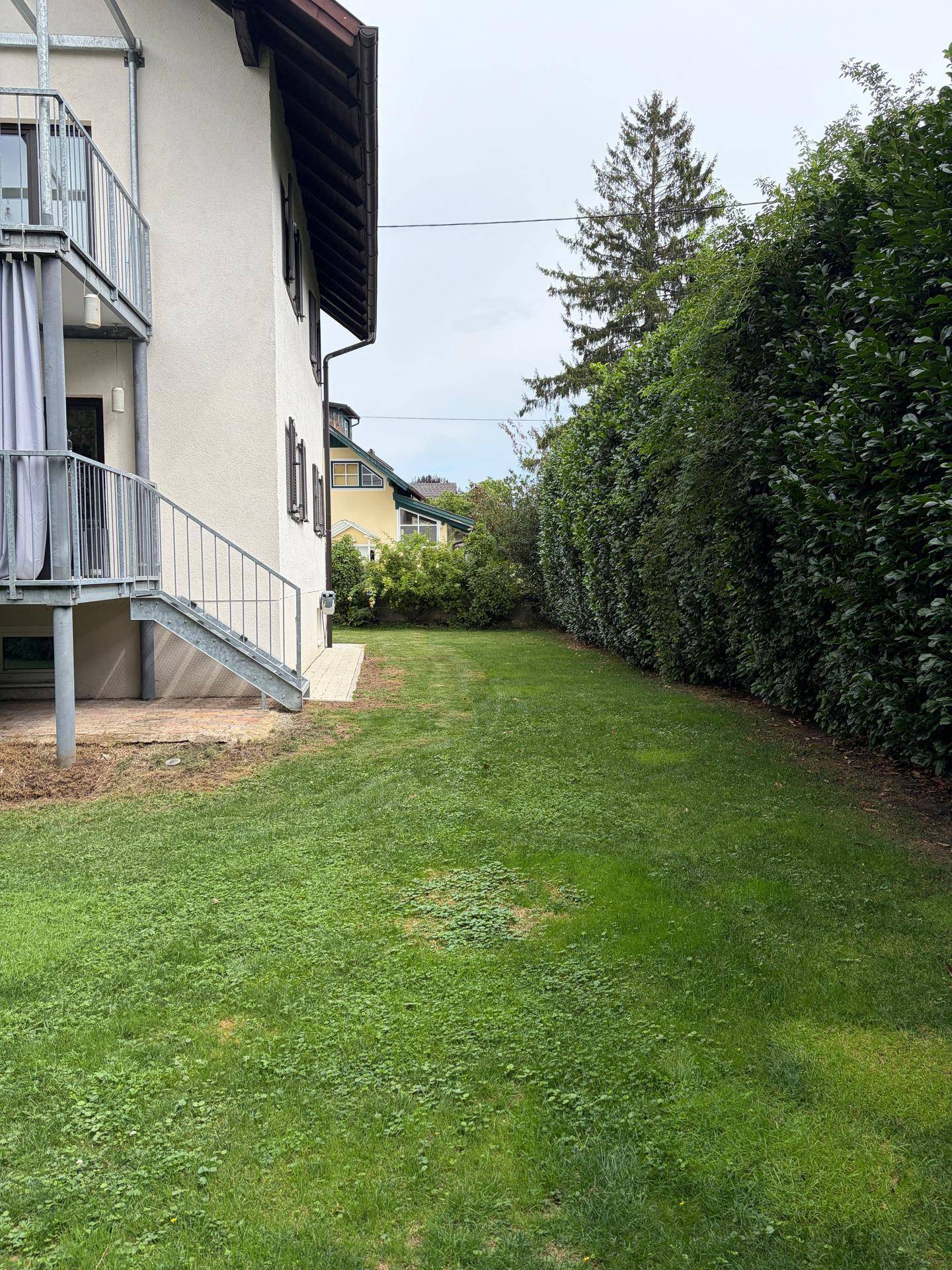 Langer, gepflegter Gartenbereich mit Rasenfläche und hoher Hecke entlang der Grundstücksgrenze.