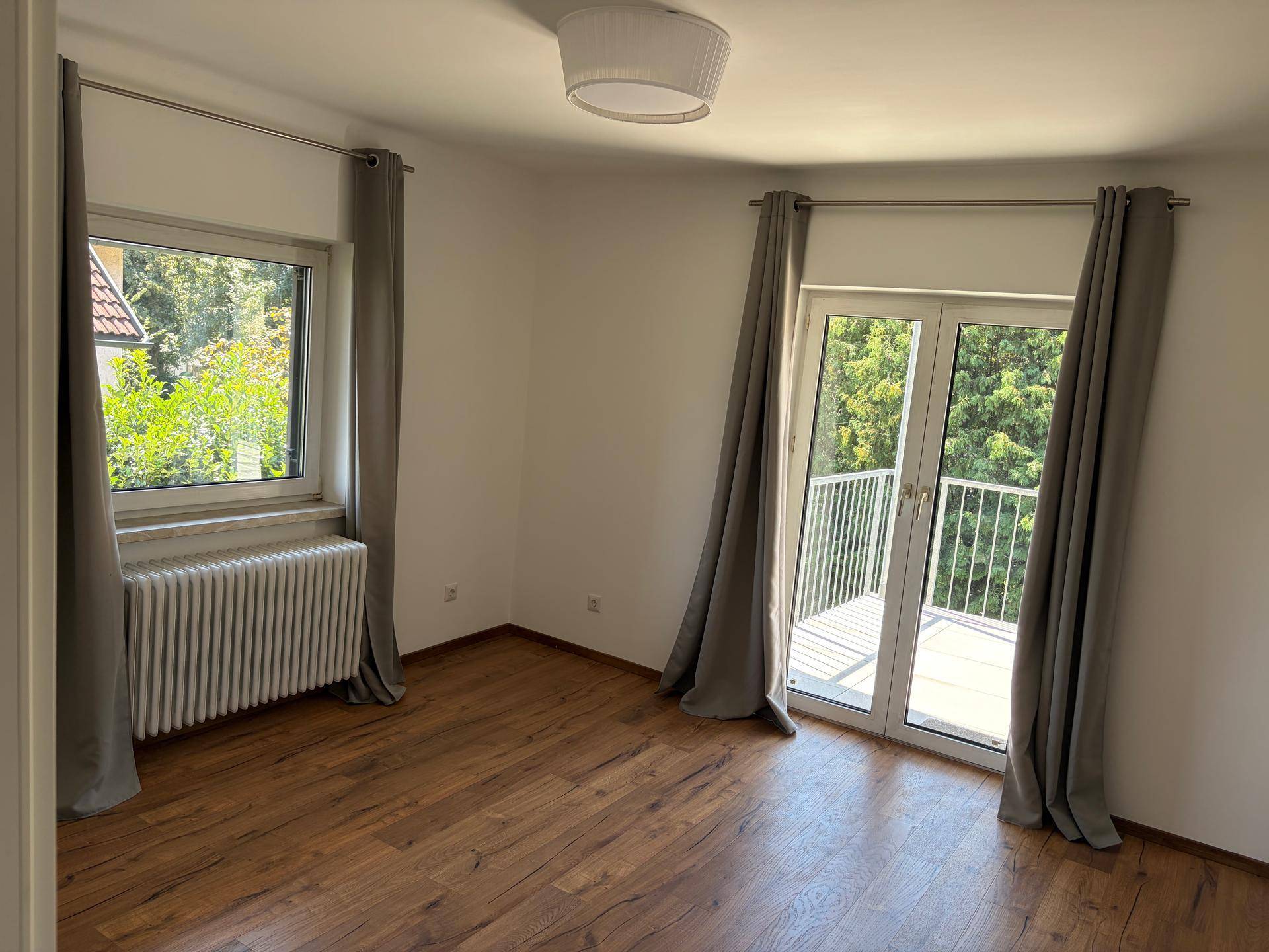 Helles Schlafzimmer mit Holzboden, großem Fenster und Zugang zu einem französischen Balkon.