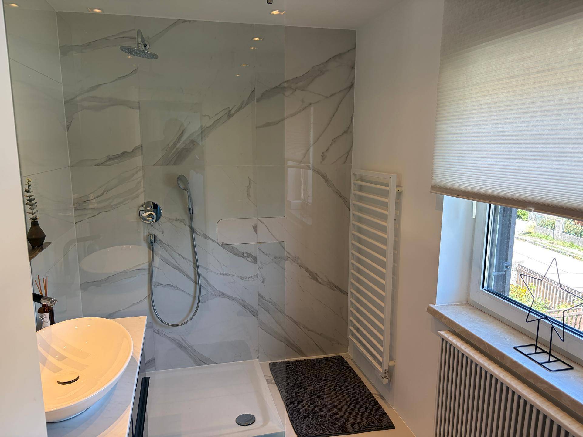 Modernes Badezimmer mit begehbarer Dusche, Marmoroptik-Fliesen und Fenster für Tageslicht.