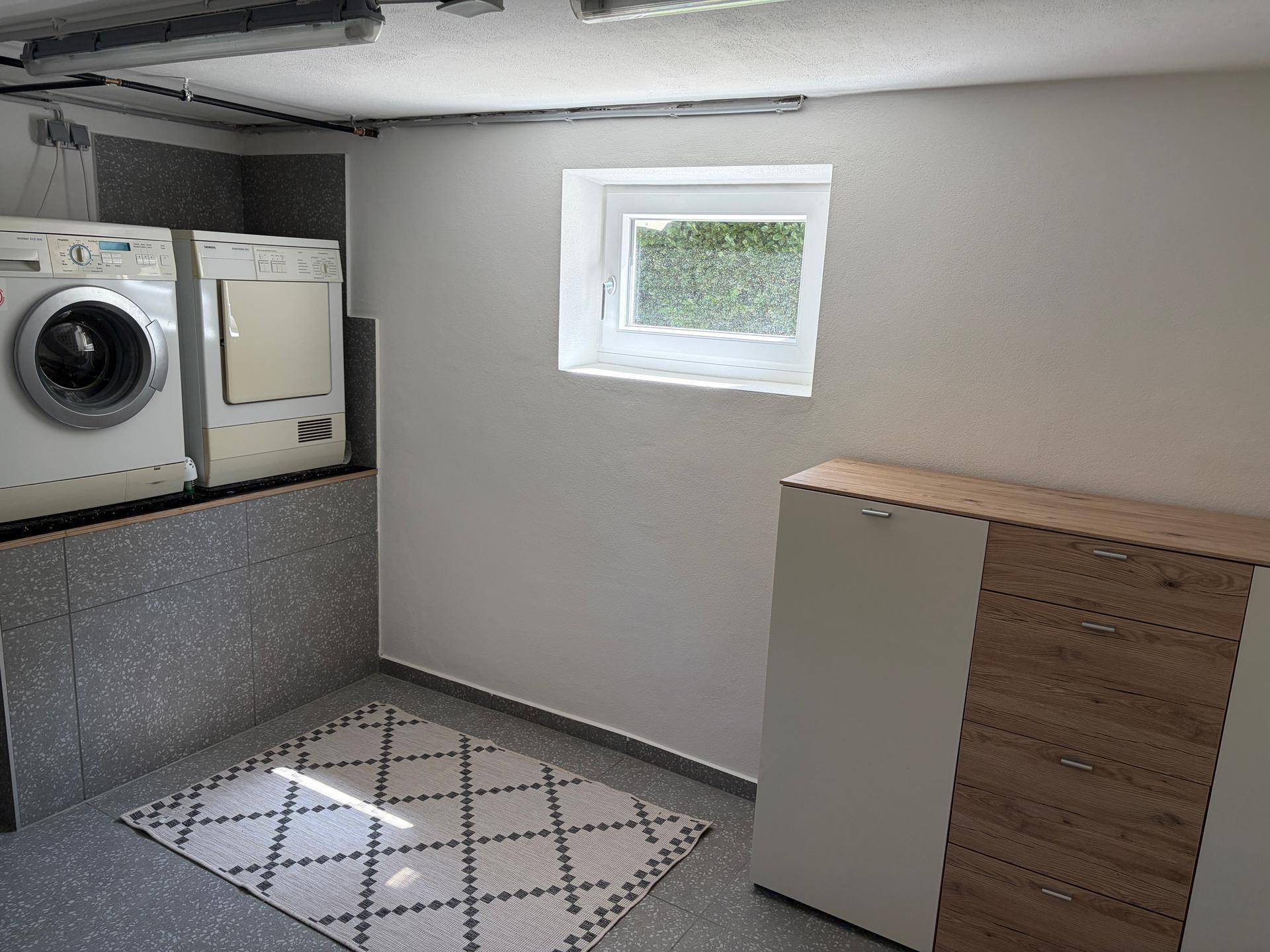 Waschküche im Keller mit Waschmaschine, Trockner und Fenster für Belüftung.
