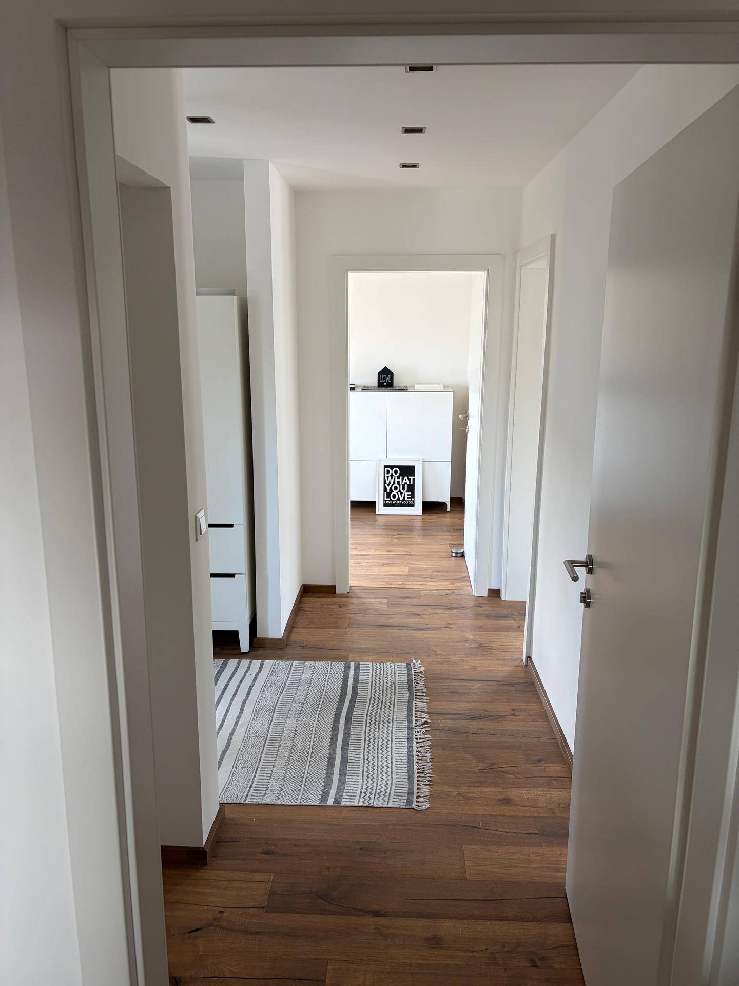 Heller Flur mit Holzparkettboden und weißer Einrichtung, der zu weiteren Räumen führt.
