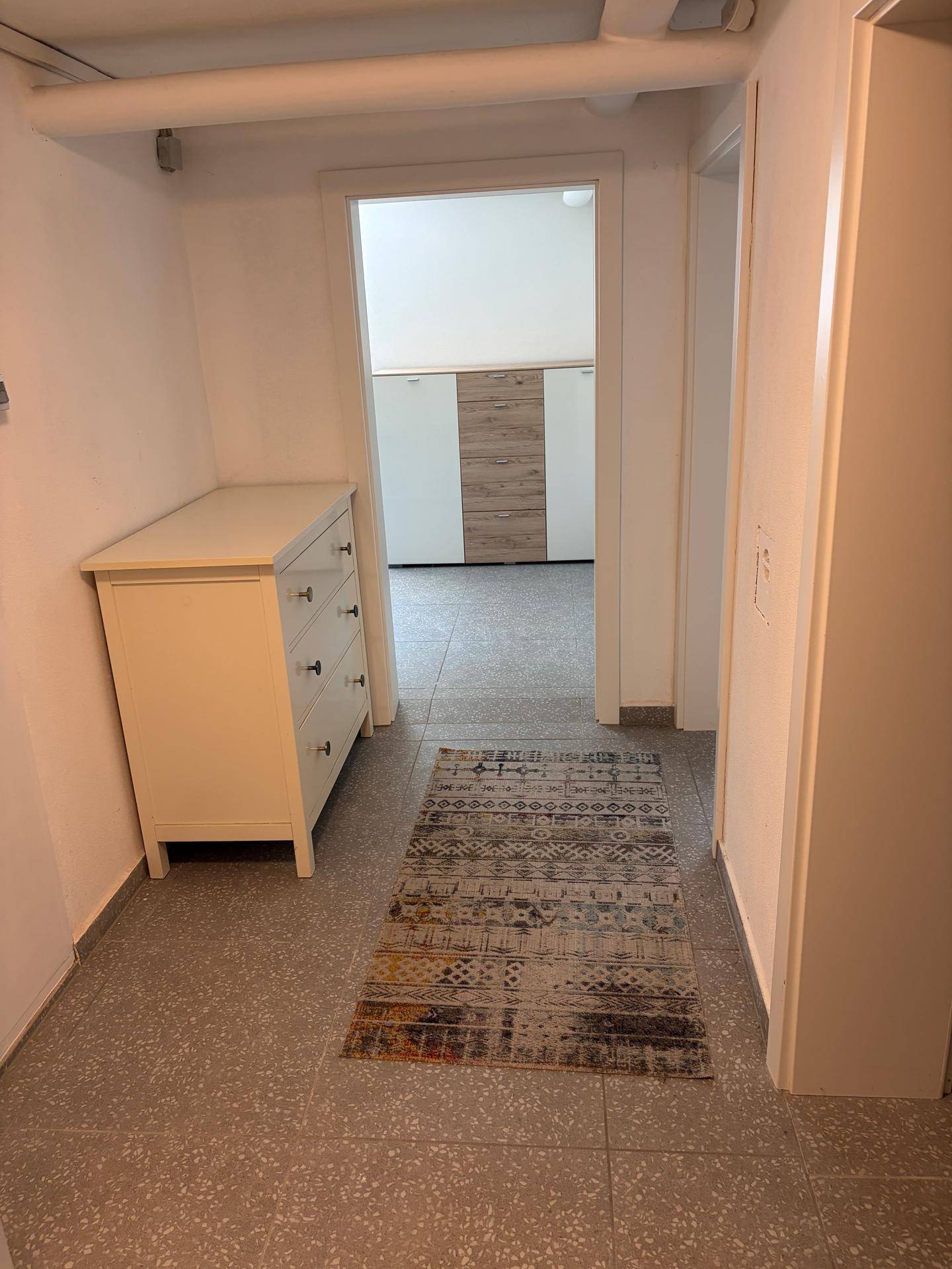Kellerflur mit Fliesenboden und weißer Kommode, der zu weiteren Kellerräumen führt.