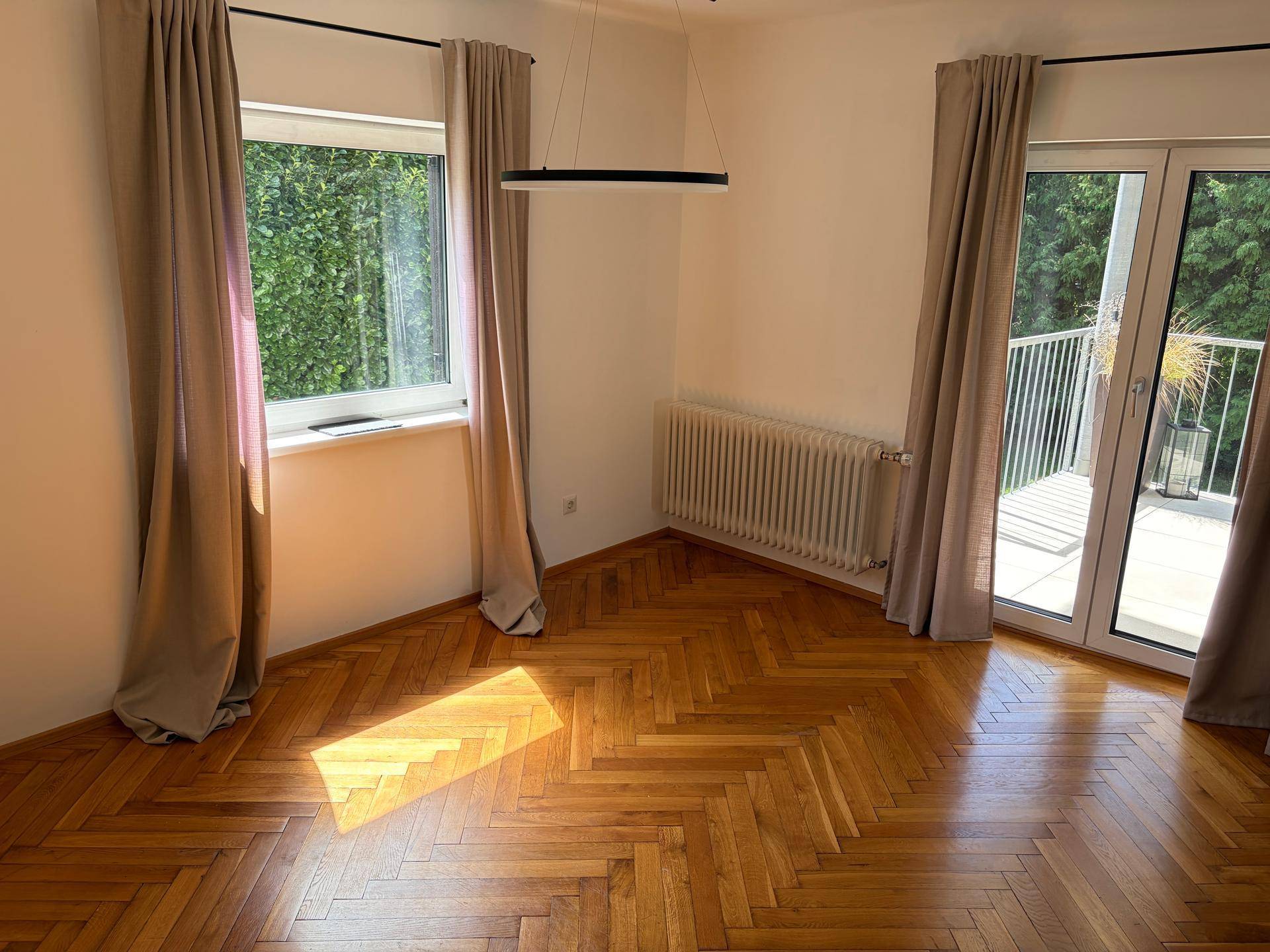 Helles Schlafzimmer mit Fischgrätparkett, großem Fenster und Zugang zu einem Balkon.