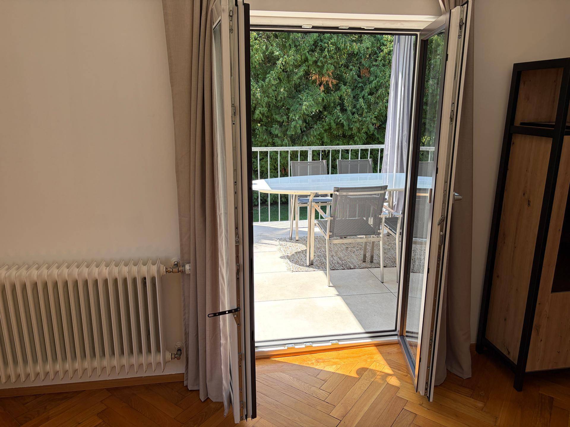 Wohnzimmer mit Fischgrätparkett und Zugang zu einer großen Terrasse mit Gartenmöbeln.