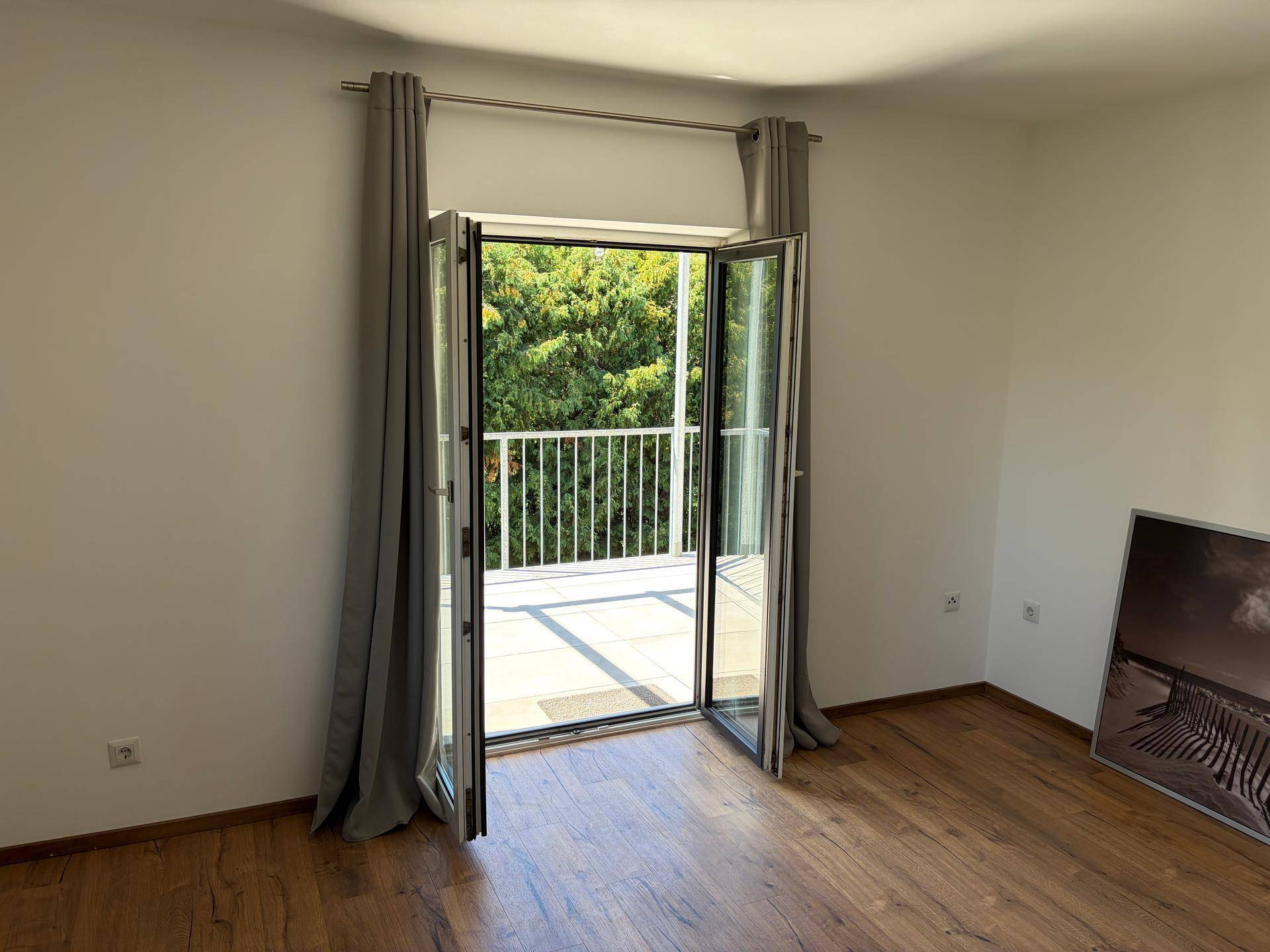 Helles Schlafzimmer mit Holzboden und Zugang zu einem Balkon mit Blick ins Grüne.