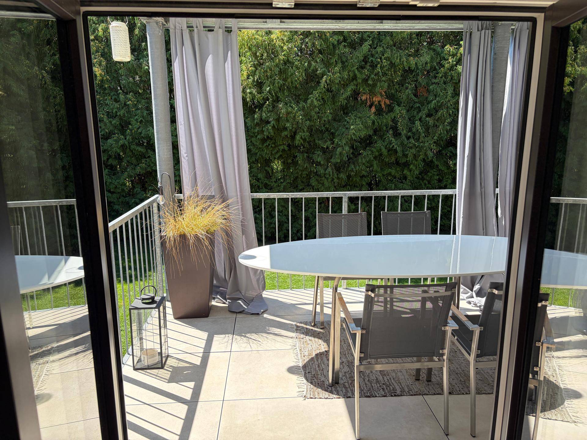 Überdachte Terrasse mit Esstisch und Pflanzen, die einen schönen Blick ins Grüne bietet.
