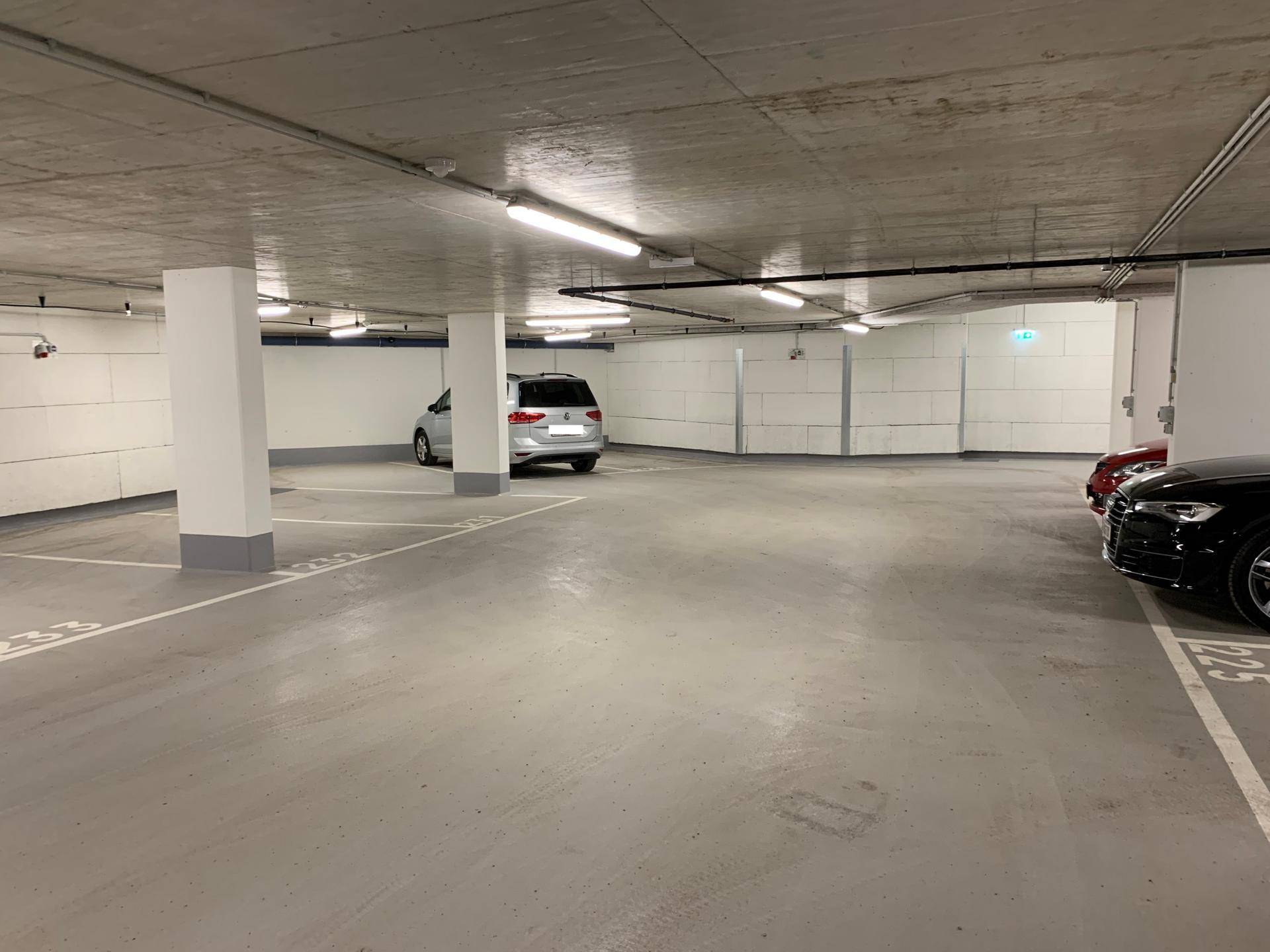 Weitläufige Tiefgarage mit mehreren Stellplätzen, Säulen und heller Beleuchtung.
