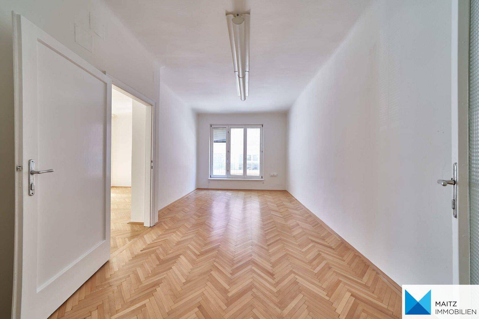 Langer, heller Flur mit Fischgrätparkett und einem Fenster am Ende, verbindet mehrere Räume.