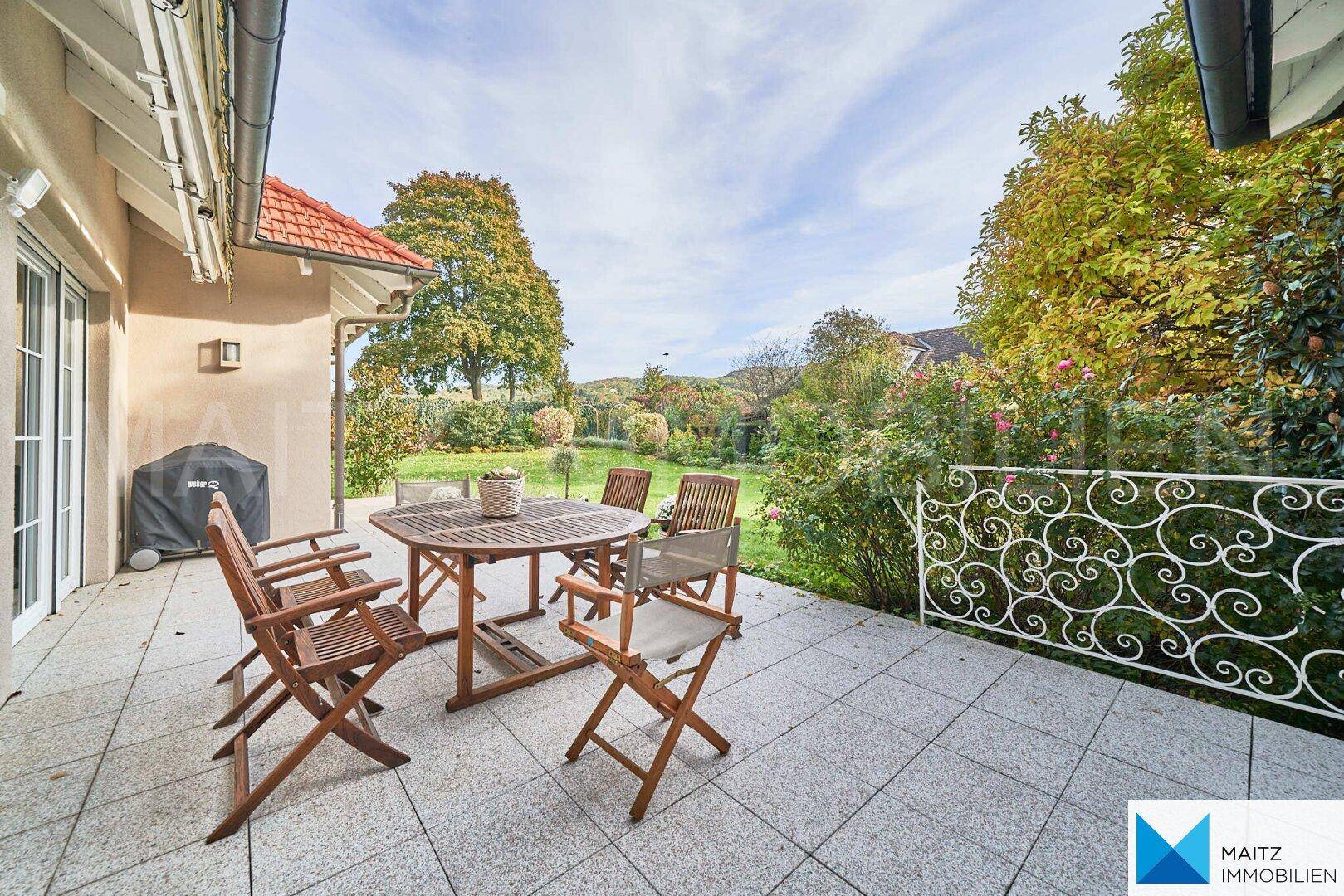 Geräumige Terrasse mit Holztisch und Stühlen, umgeben von einem grünen Garten.