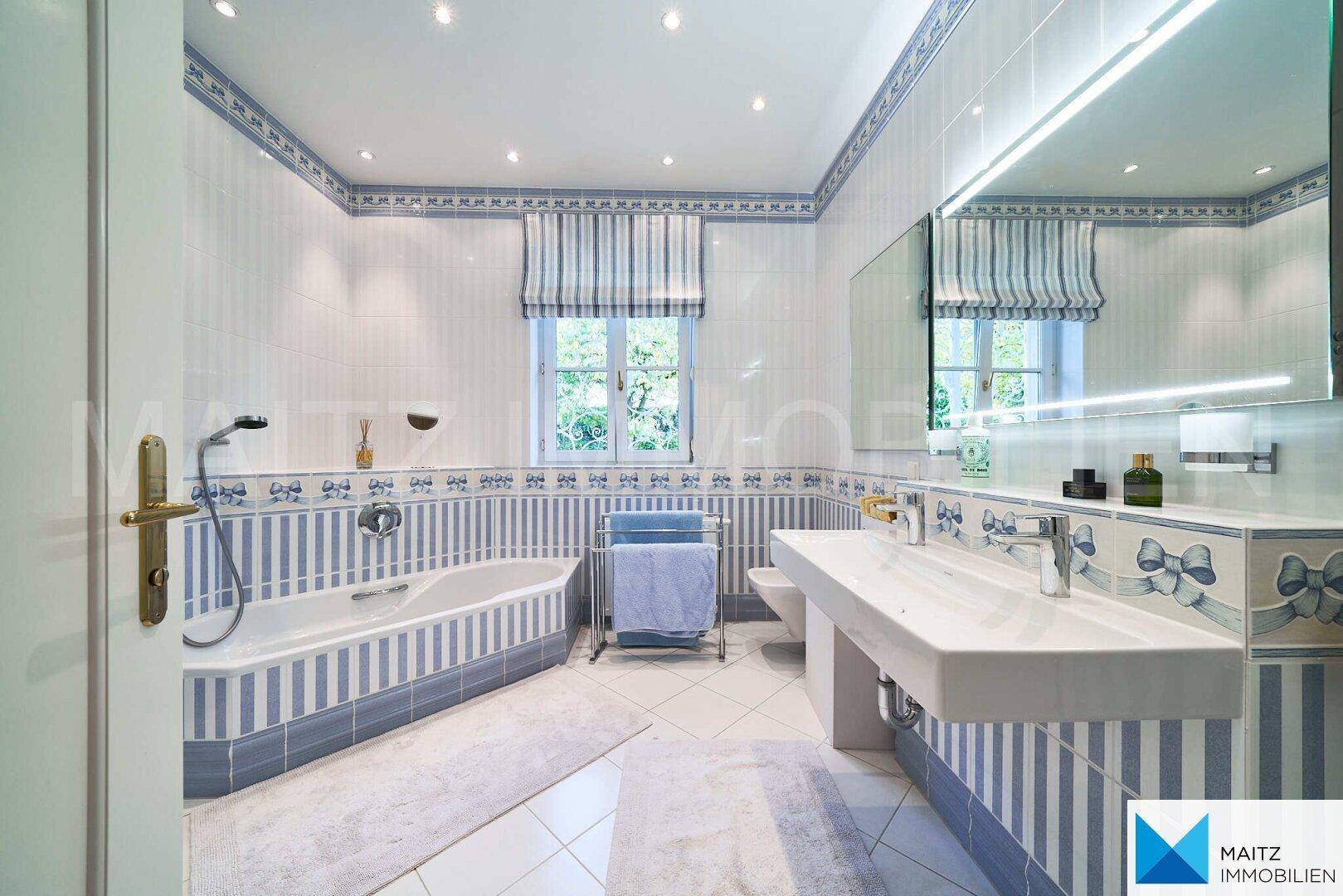 Badezimmer mit blauen und weißen Fliesen, Badewanne, Waschtisch und Fenster.