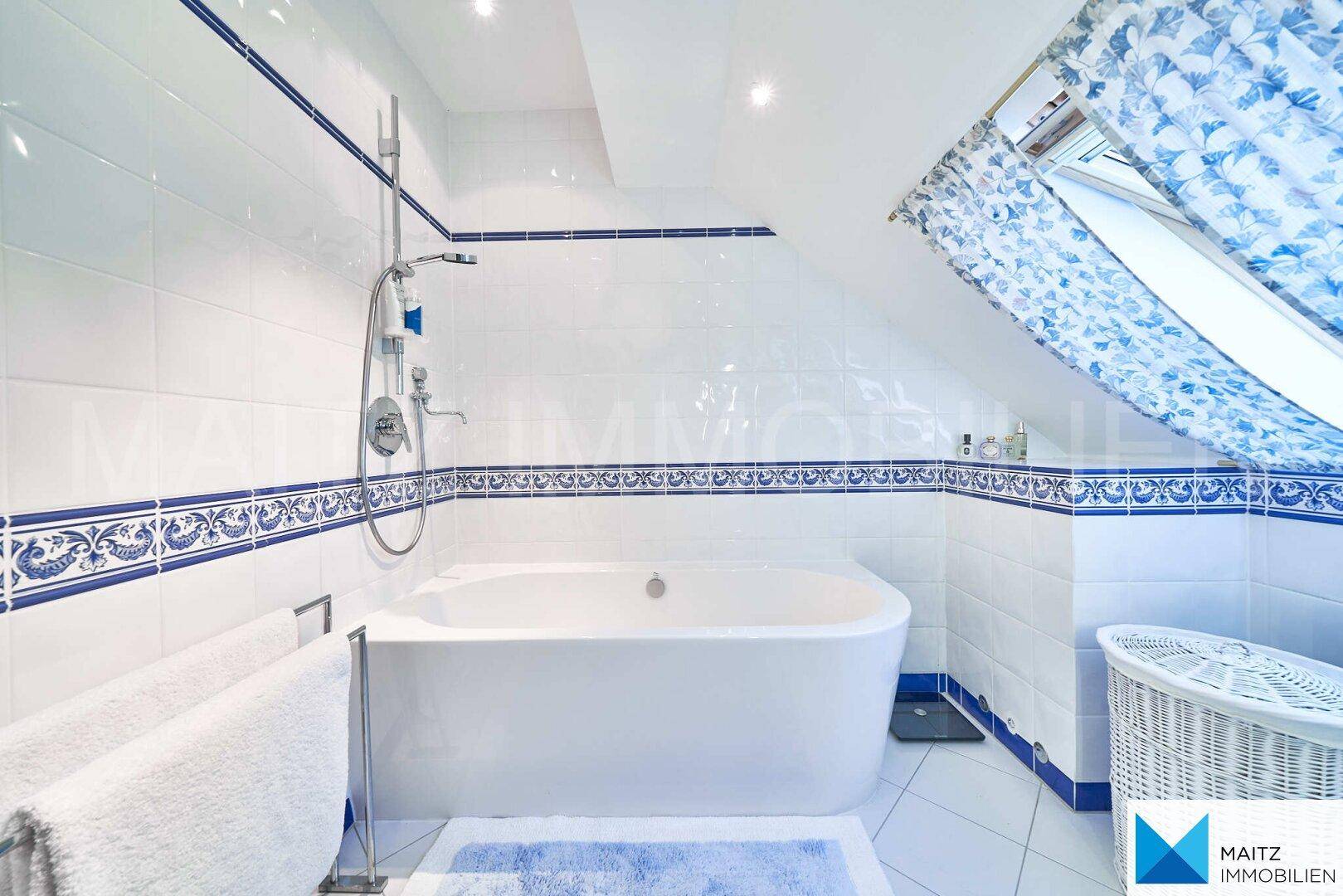 Badewanne im Dachgeschossbad mit blauen und weißen Fliesen und Schrägdach.
