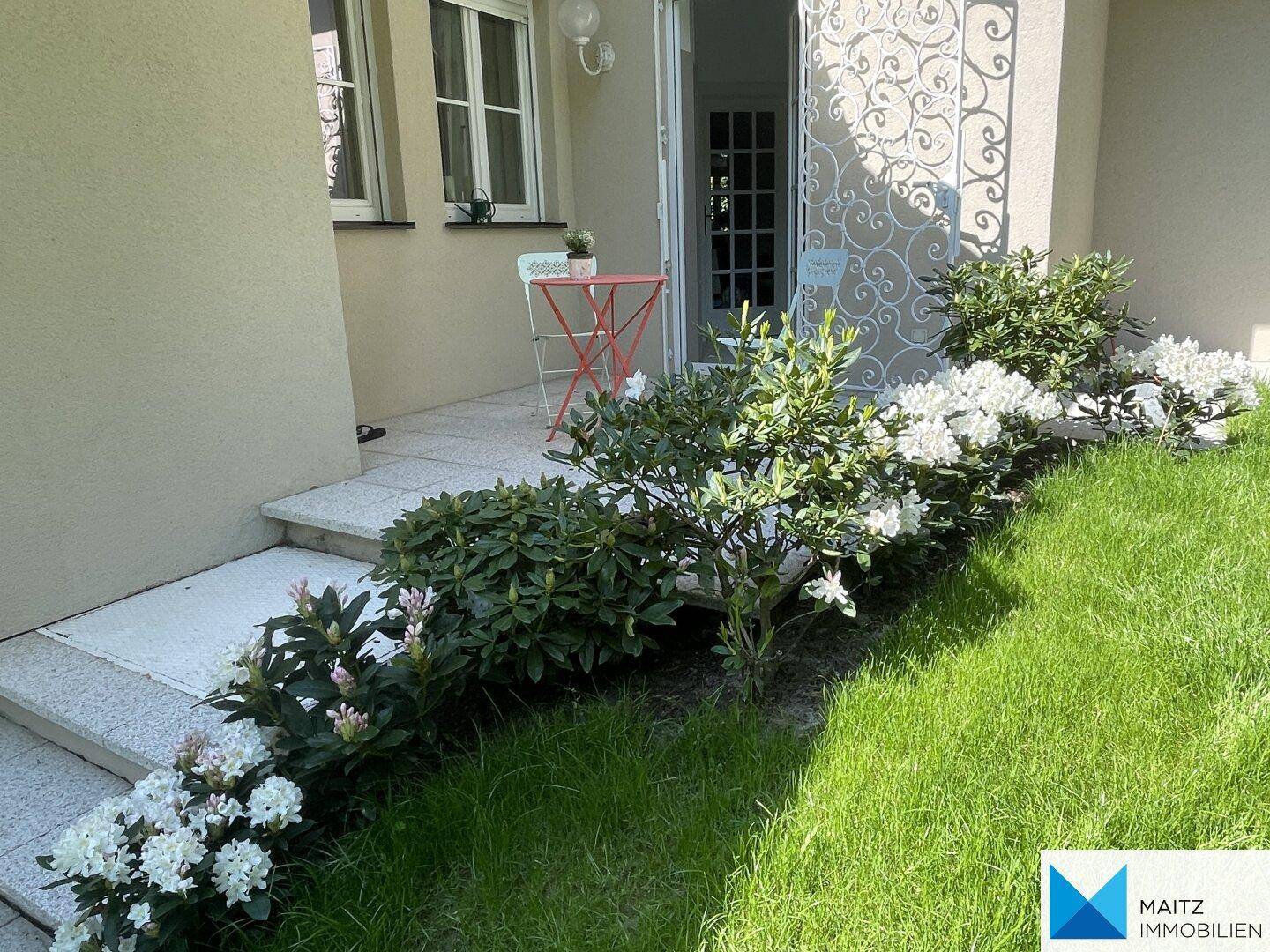 Kleiner Terrassenbereich mit Rasen und blühenden Pflanzen.