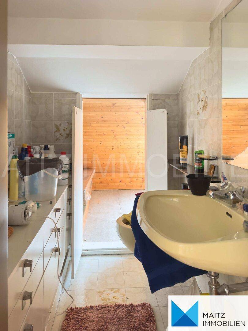Badezimmer mit Waschtisch und hellen Fliesen, angrenzend an einen Holzbereich.