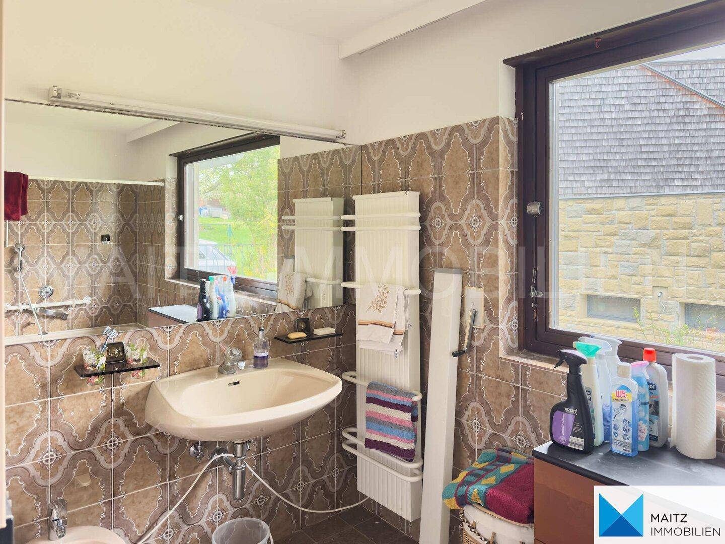 Badezimmer mit Waschtisch, großem Spiegel und braunen Fliesen im Retro-Design.