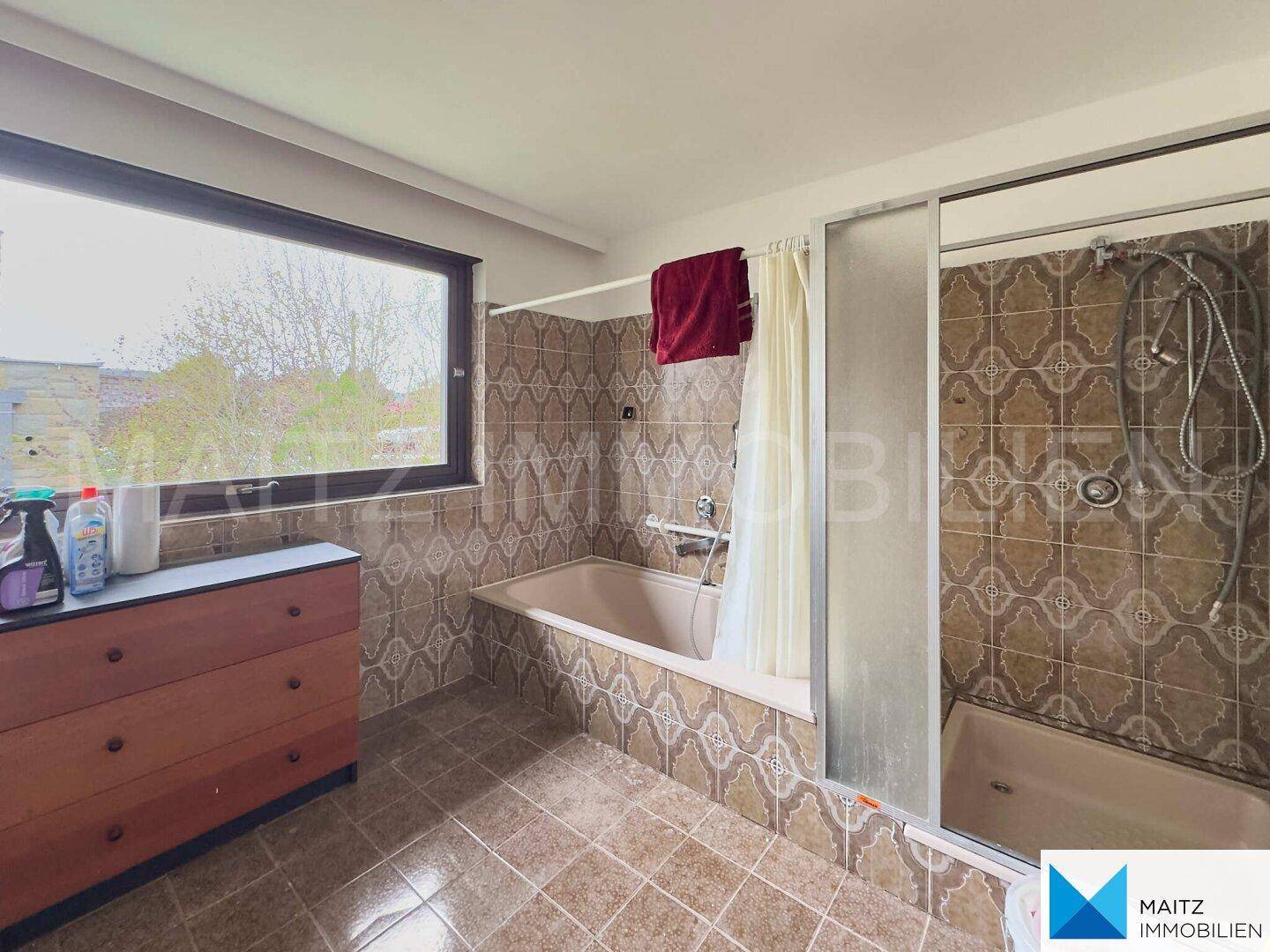 Badezimmer im 80er-Jahre-Stil mit Badewanne, Dusche und gemusterten Fliesen.