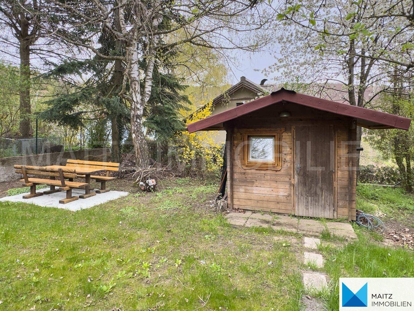 Idyllischer Gartenbereich mit einer kleinen Holzhütte und einer rustikalen Holzbank.
