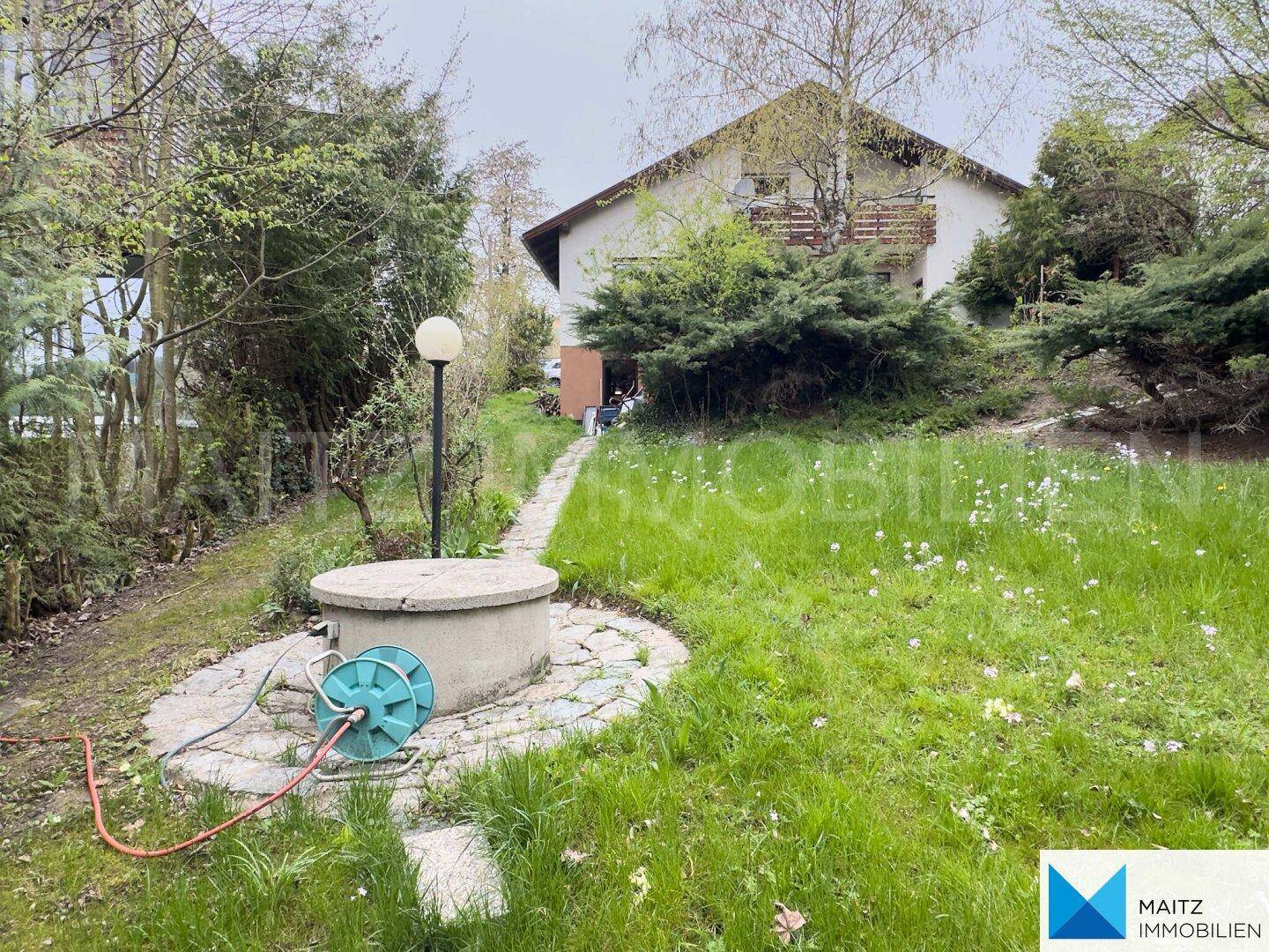 Gepflegter Gartenbereich mit Rasenfläche, Gartenweg und einem dekorativen Brunnen vor dem Haus.