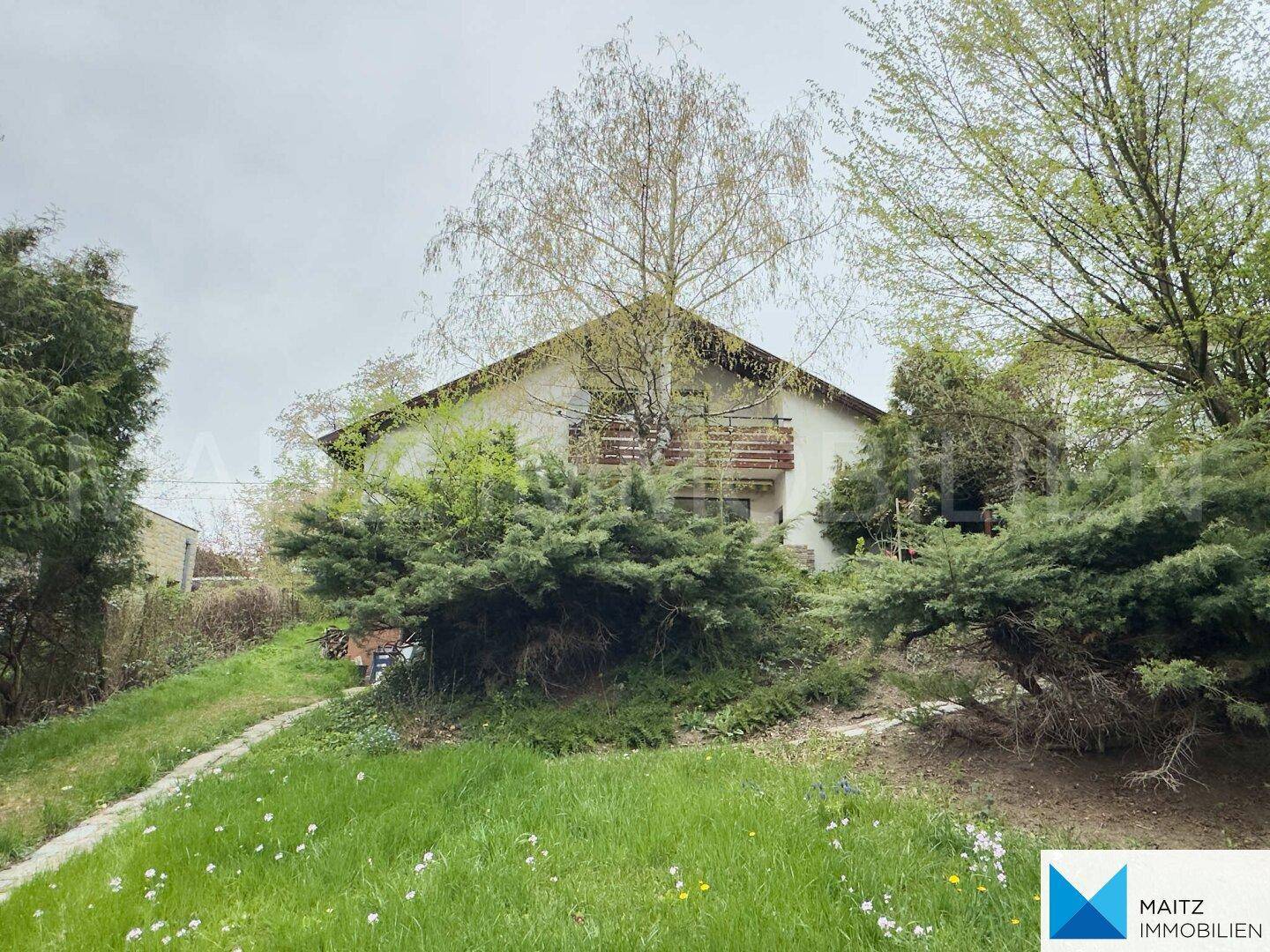 Ansicht des Hauses von der Gartenseite mit Balkon und umgebender üppiger Vegetation.
