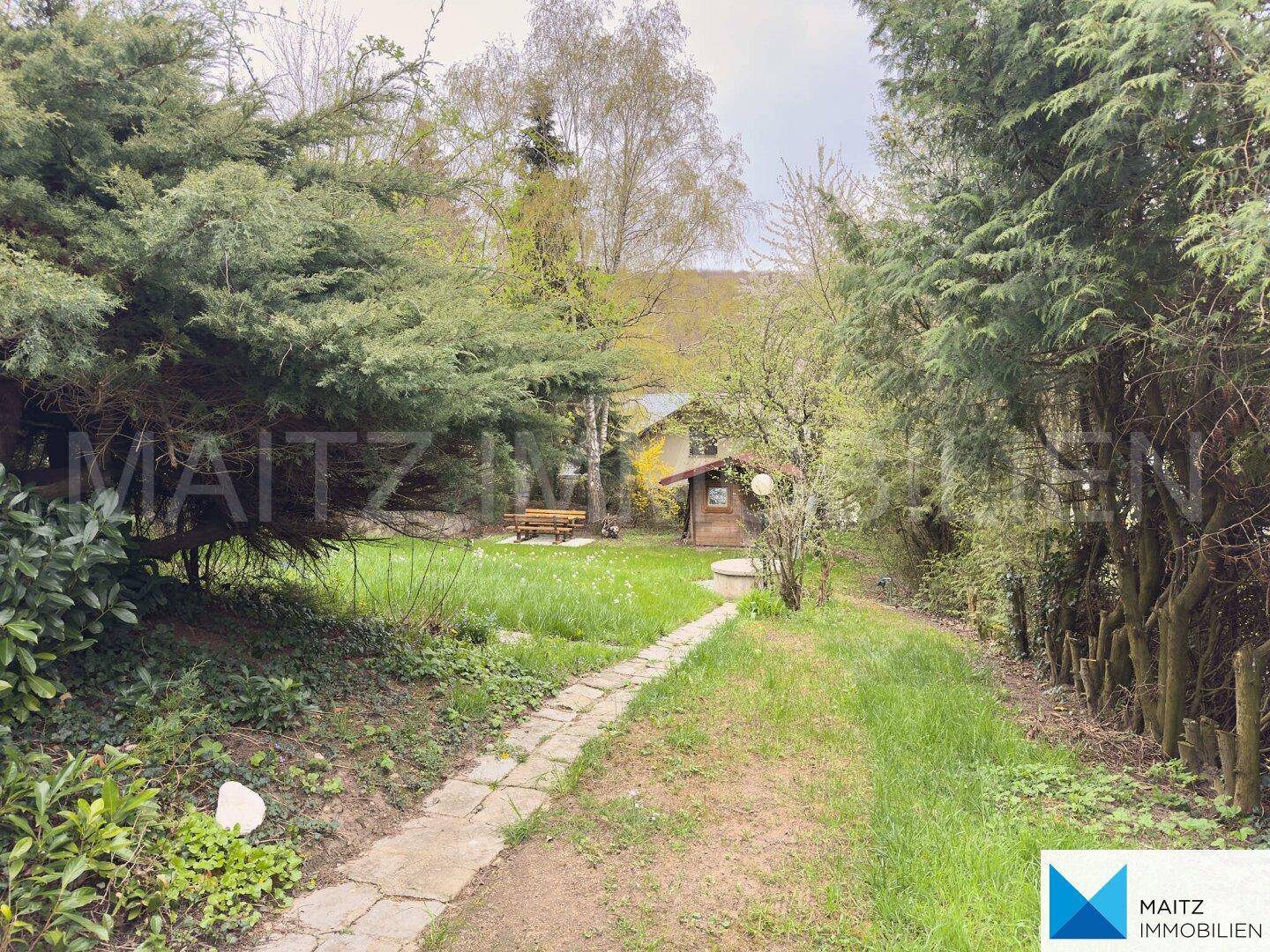 Gartenweg schlängelt sich durch die grüne Landschaft, führt zum Haus und einer kleinen Hütte.