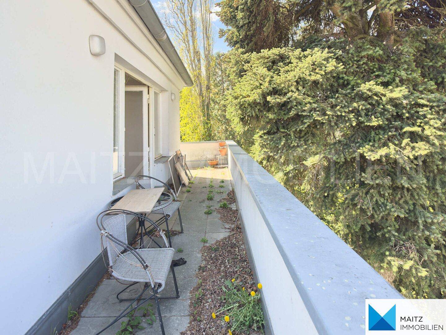 Schmaler Balkon mit Sitzgelegenheiten und üppigem Baumbestand, der Privatsphäre und Schatten bietet.