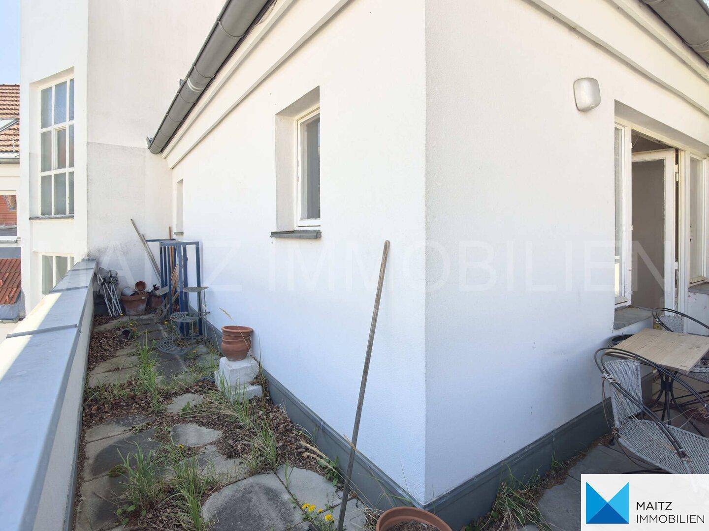 Ecke des Gebäudes mit einem Balkon, der von Bäumen umgeben ist und Potenzial für Gestaltung bietet.