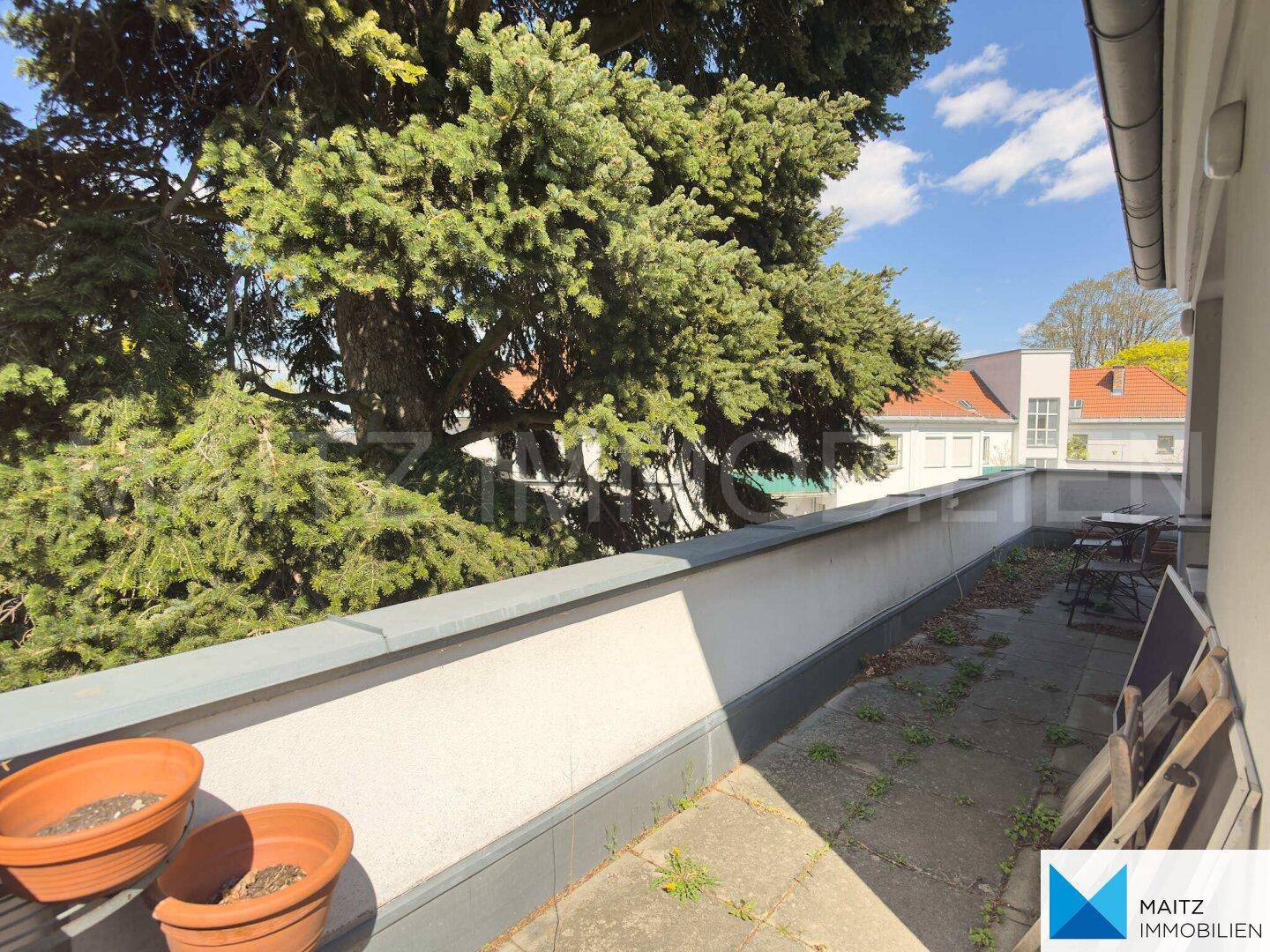 Langer Balkon mit Blick ins Grüne und auf umliegende Dächer, ideal zum Entspannen im Freien.