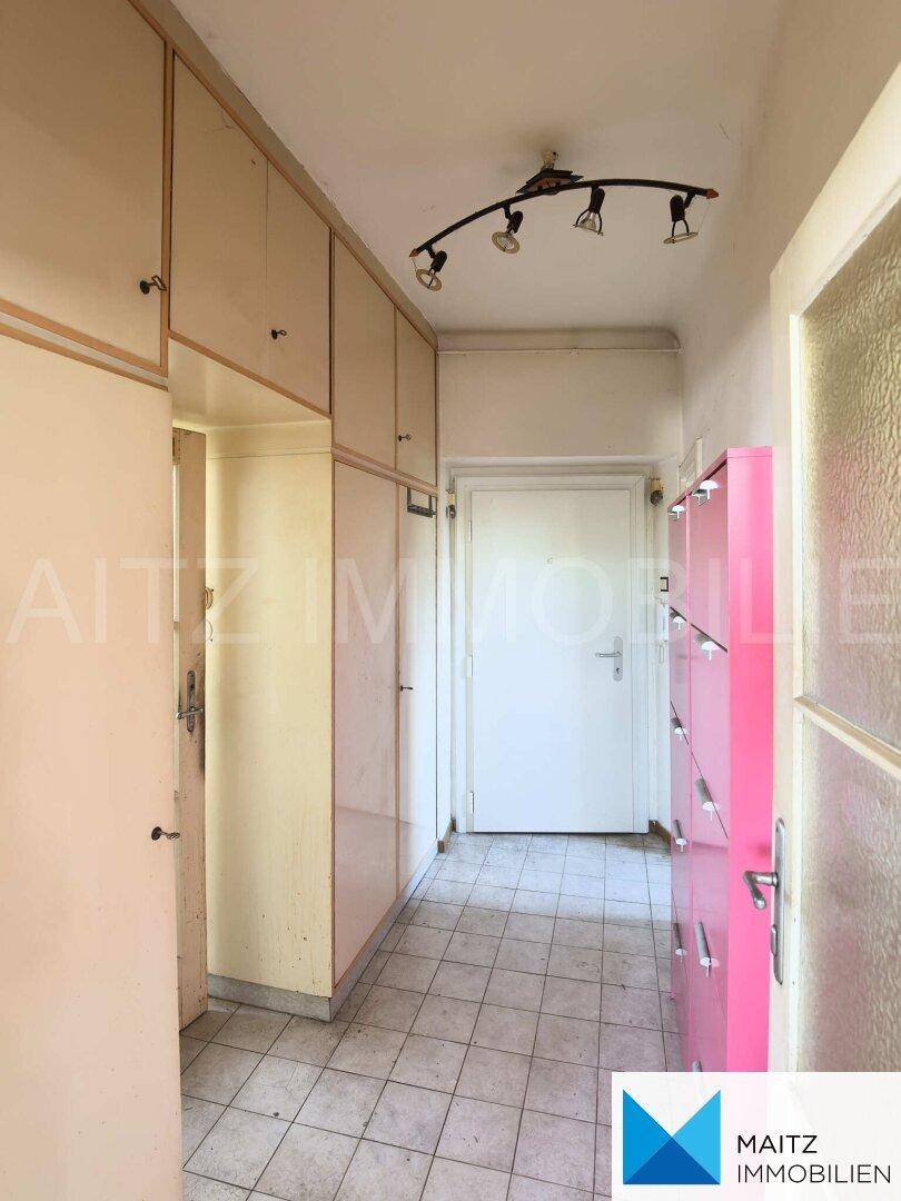 Langer Flur mit zahlreichen Einbauschränken und Fliesenboden, führt zum Eingang der Wohnung.