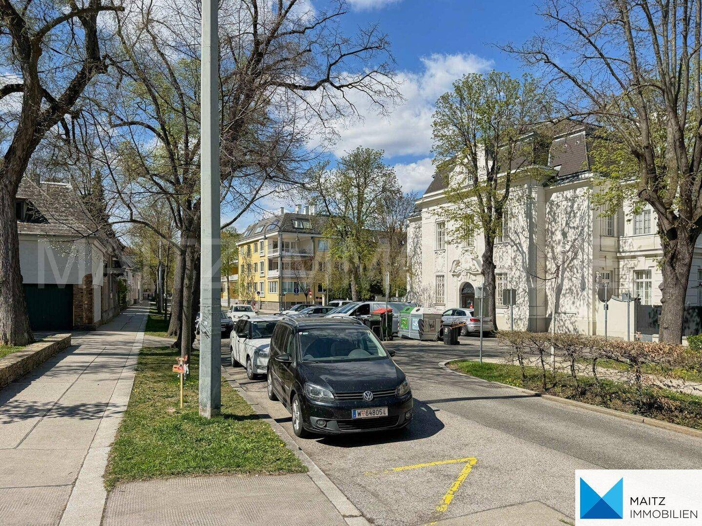 Wohngegend mit gepflegten Gebäuden, Bäumen und parkenden Fahrzeugen entlang der Straße.